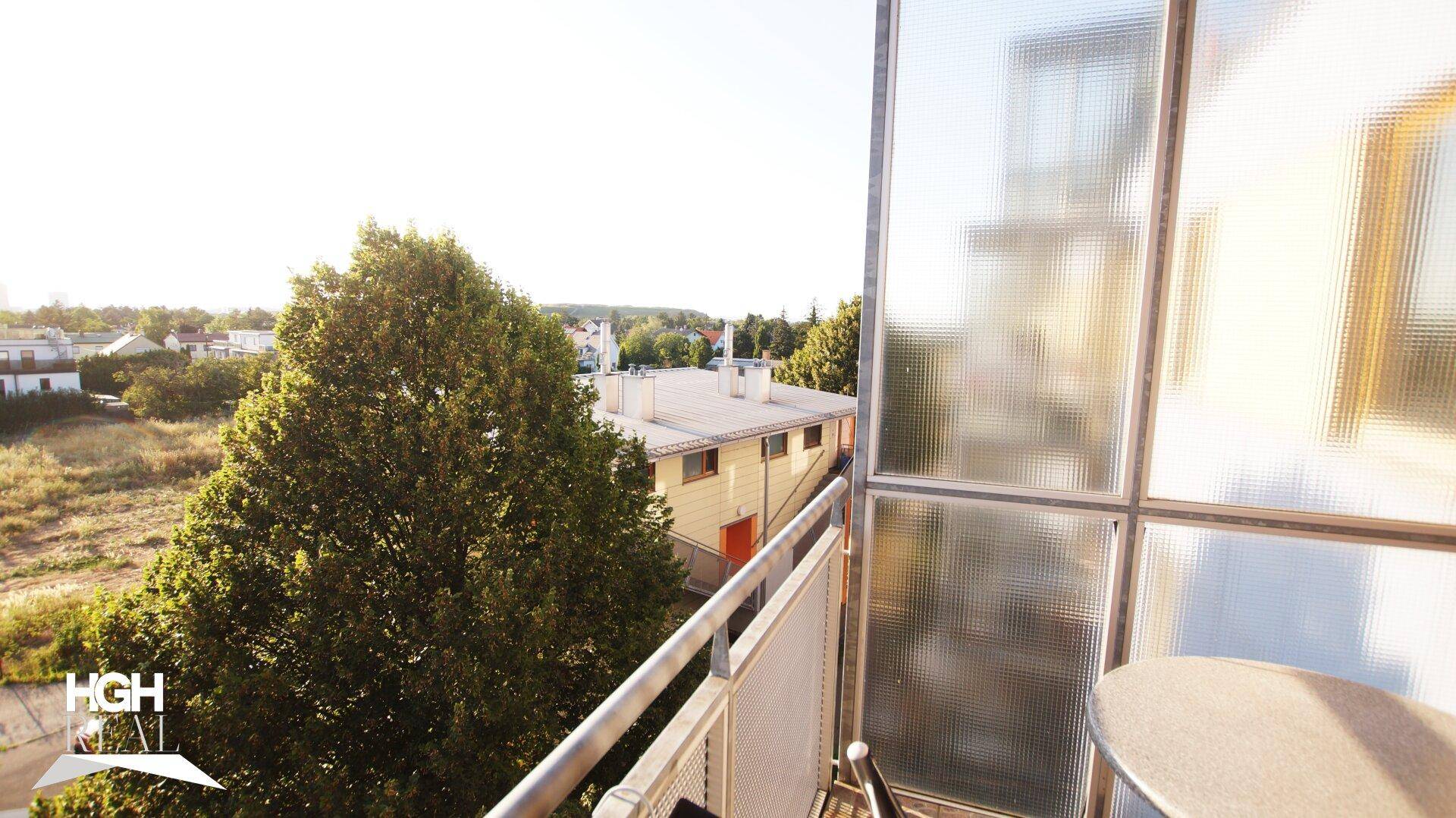 Balkon mit Sitzgelegenheit, umgeben von Bäumen und Blick auf die Umgebung.