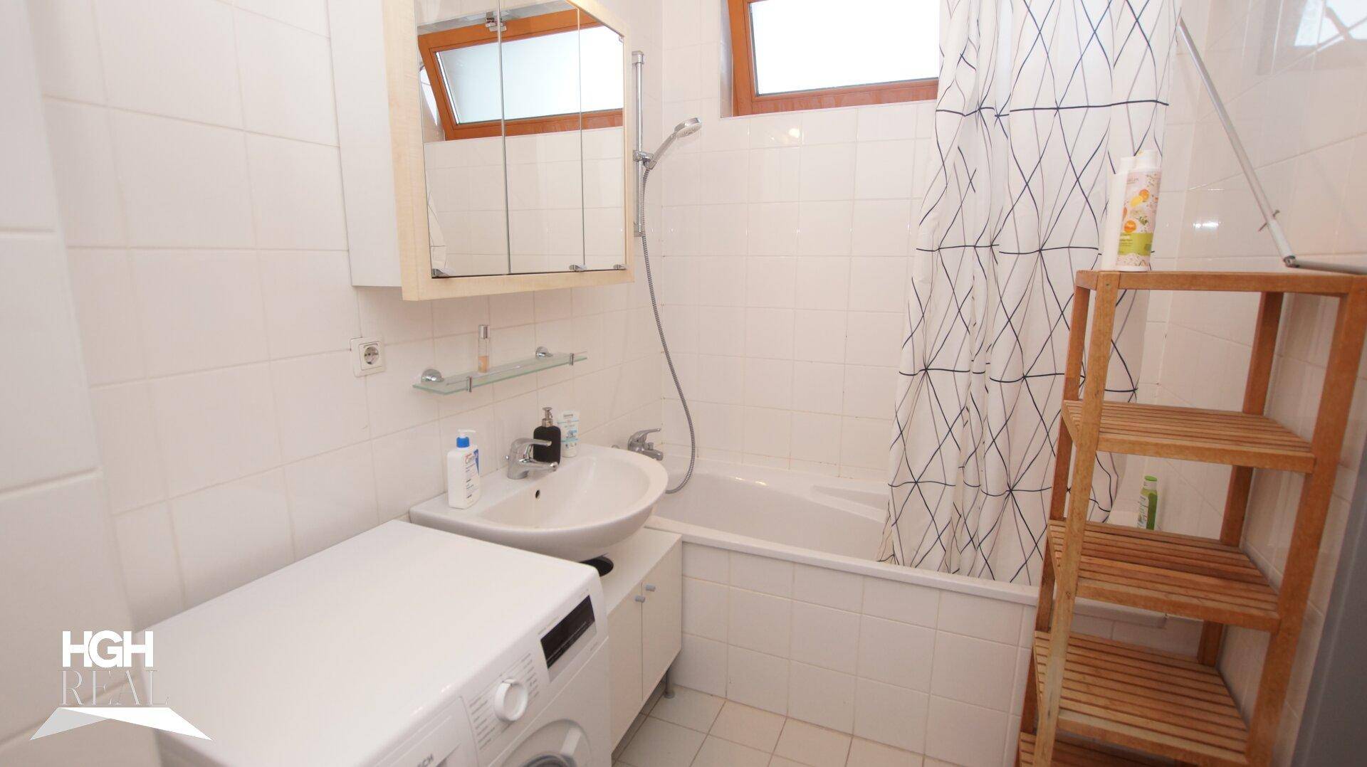 Helles Badezimmer mit Badewanne, Duschvorhang, Waschbecken und Fenster.