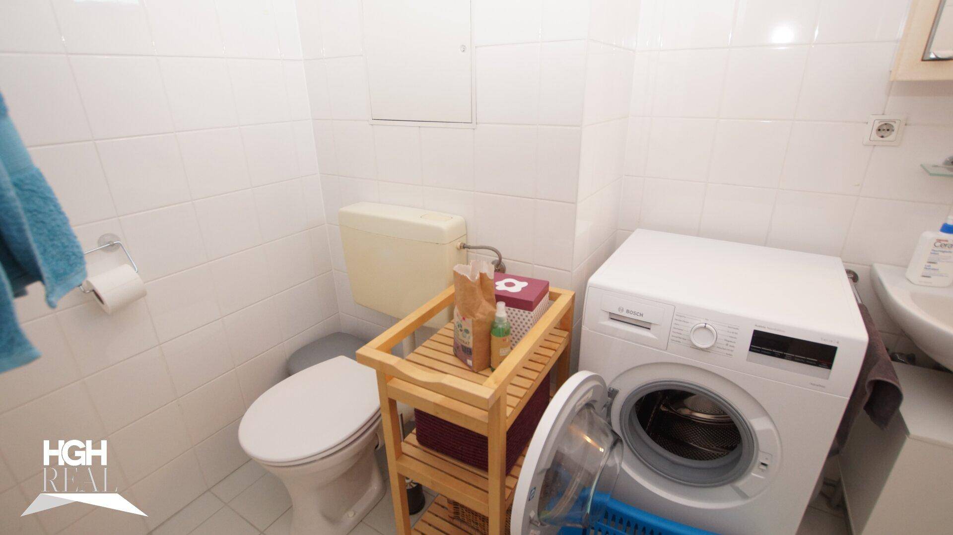 Badezimmer mit WC, Waschmaschine und weißen Fliesen.