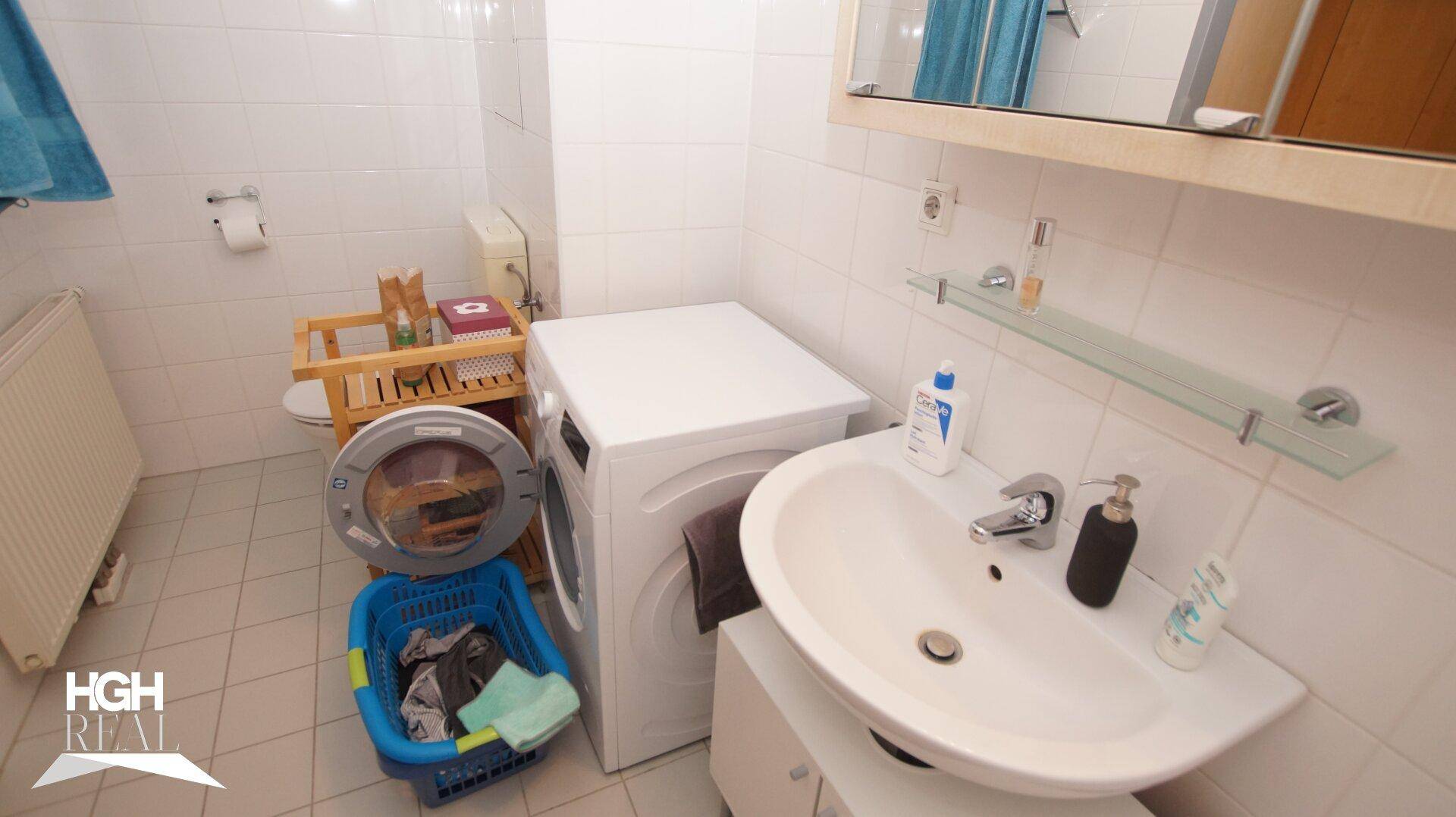 Badezimmer mit WC, Waschbecken, Waschmaschine und weißen Fliesen.
