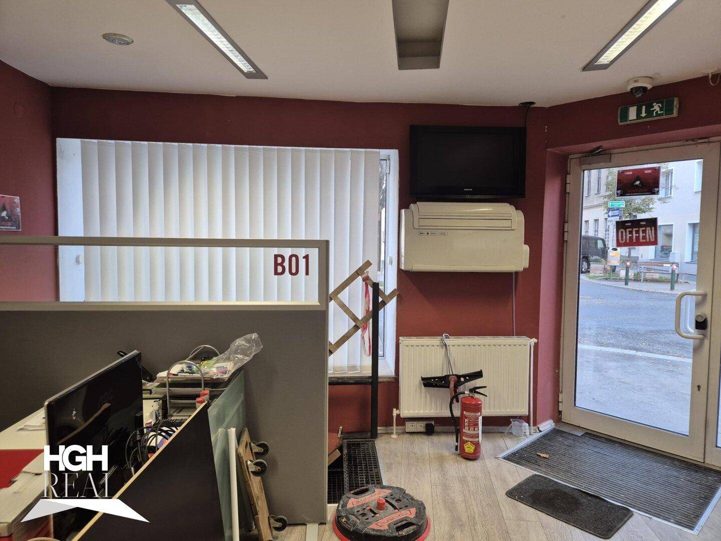 Eingangsbereich eines Geschäftsraums mit Glastür zur Straße und Fenster mit Jalousien.