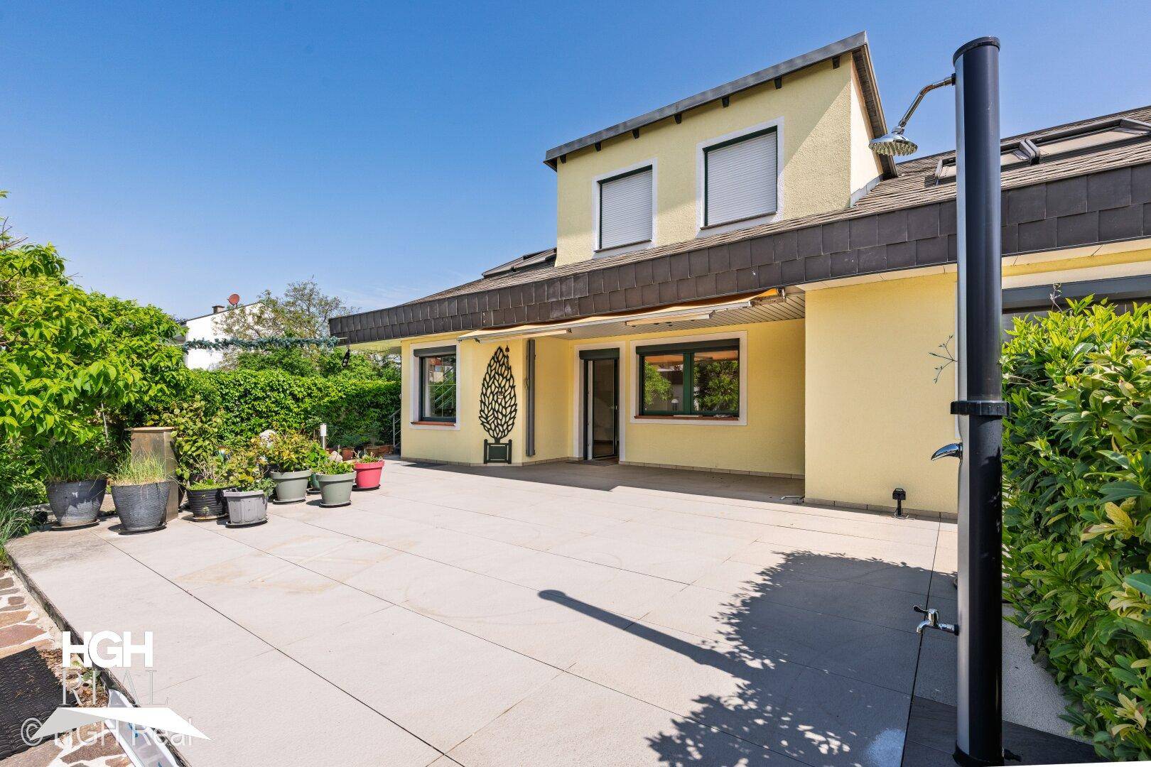 Große gepflasterte Terrasse mit Außendusche und Blick auf das Haus.