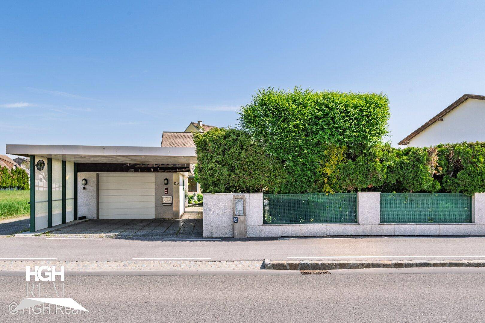 Moderne Garagenzufahrt mit Carport und gepflegter Hecke zur Straße hin.