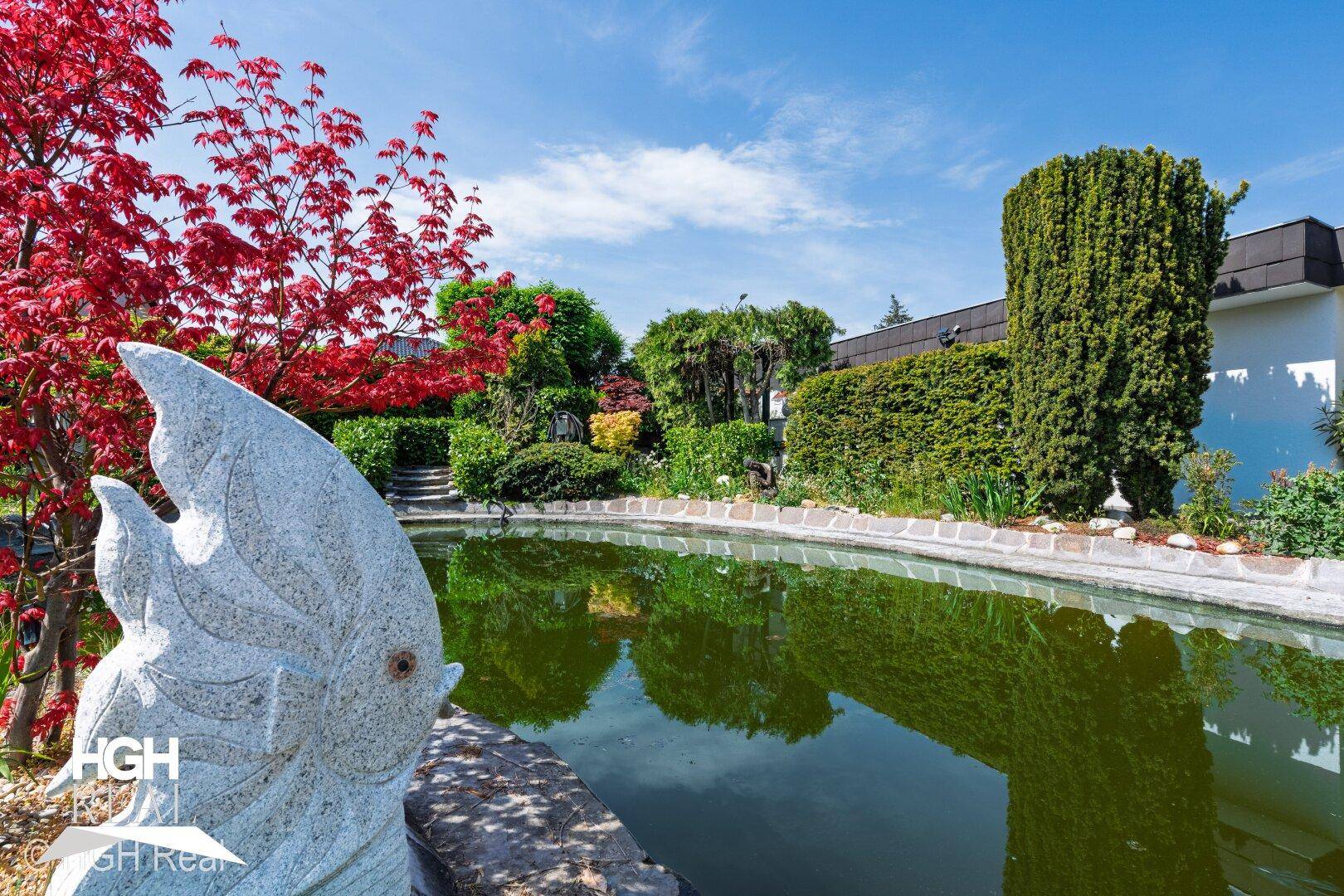 Dekorativer Teich im Garten mit üppiger Bepflanzung und Skulptur.