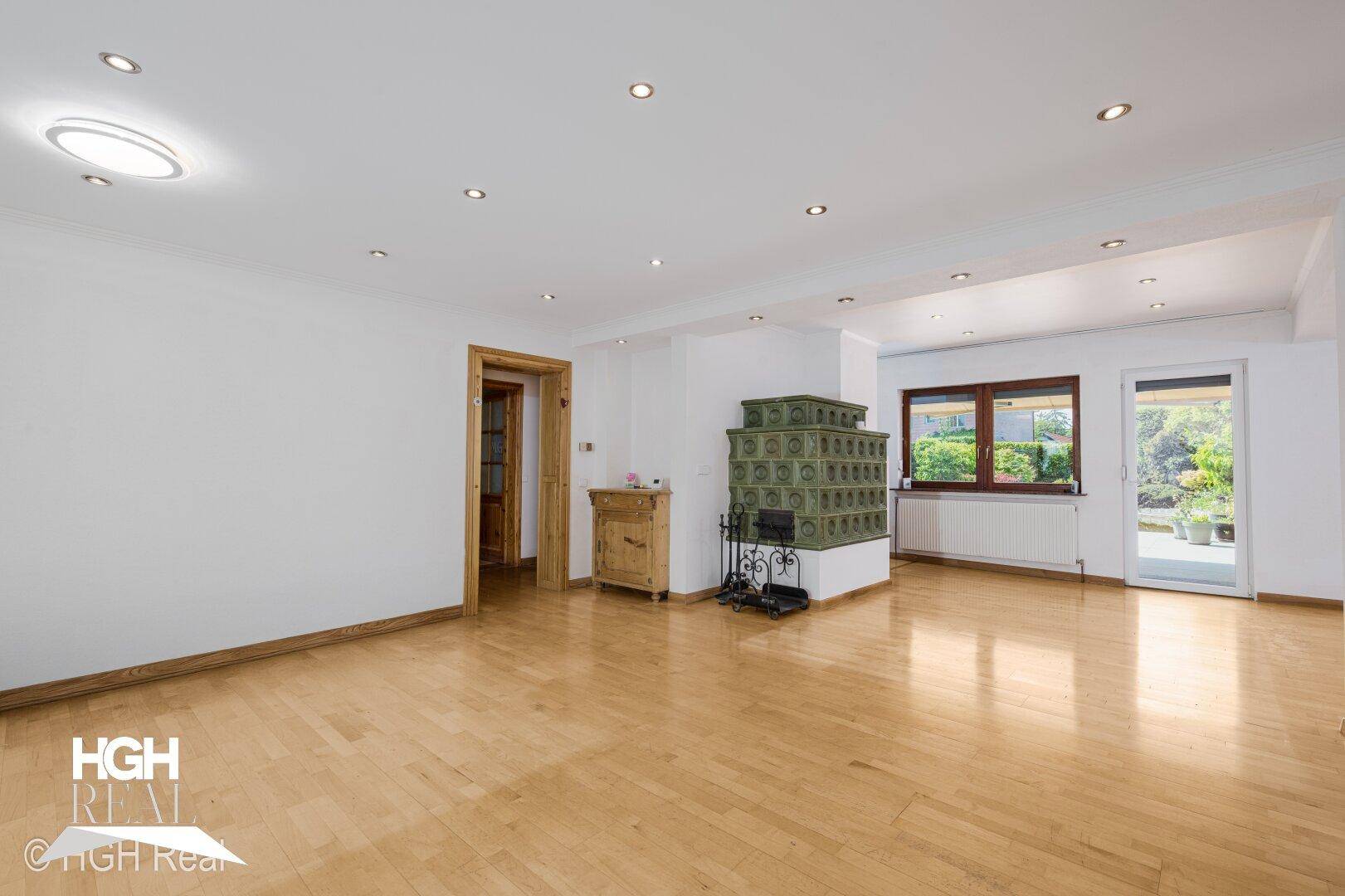 Geräumiges Wohnzimmer mit Parkettboden, traditionellem Kachelofen und Zugang zum Außenbereich.