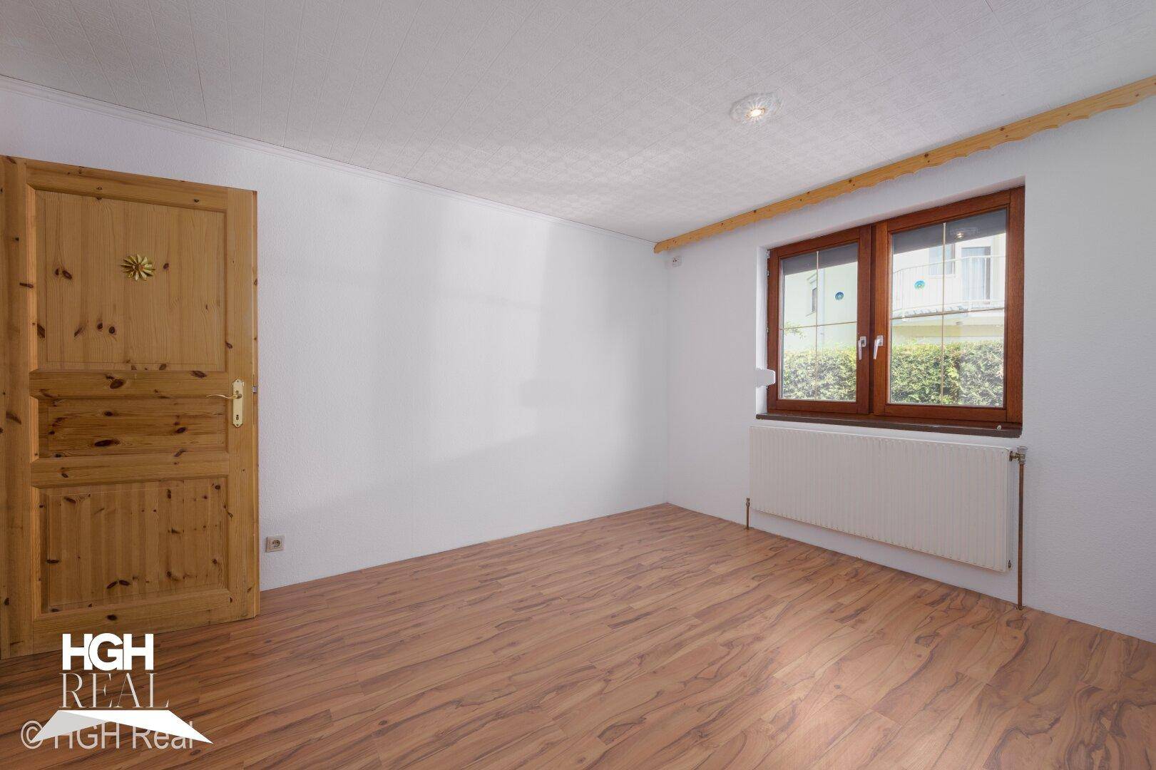 Helles Schlafzimmer mit Laminatboden und Fenster mit Blick ins Grüne.