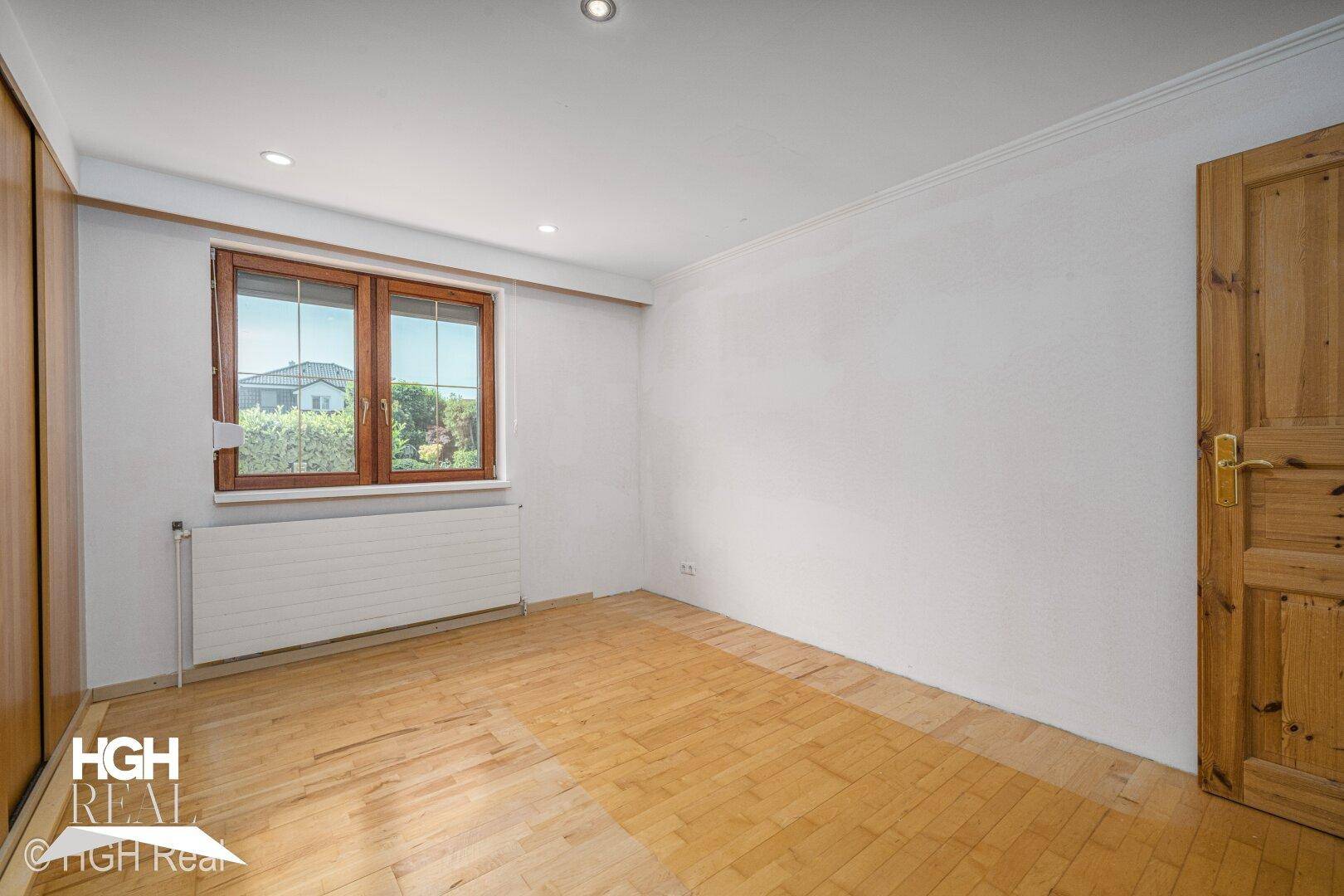 Geräumiges Schlafzimmer mit Parkettboden, großem Fenster und Einbauschrank.