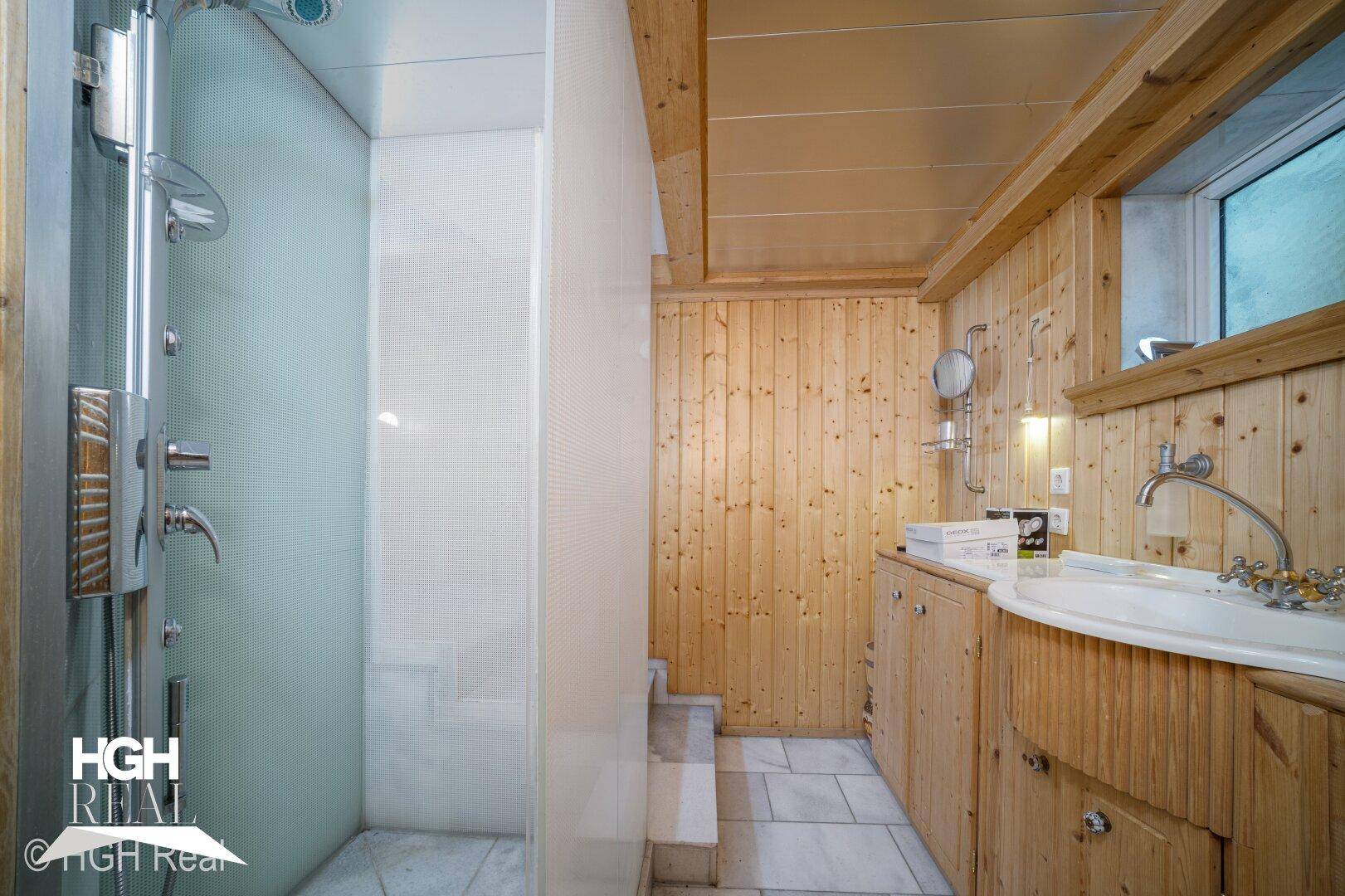 Gemütliches Badezimmer mit Holzverkleidung, Duschkabine und Waschtisch.