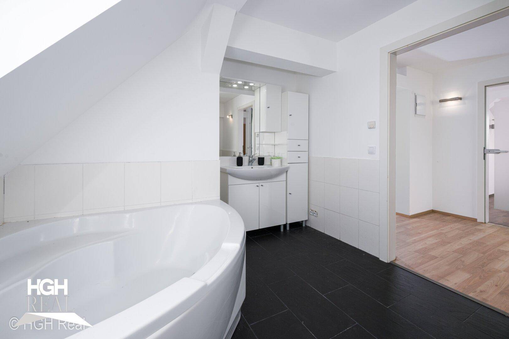 Geräumiges Dachgeschossbad mit Badewanne, Waschtisch und weiß gefliesten Wänden.