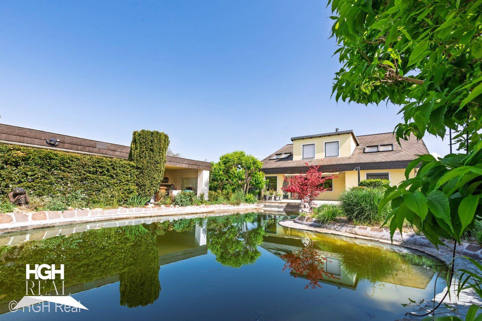 Weitläufiger Garten mit großem Teich und Blick auf die Hausfassade.