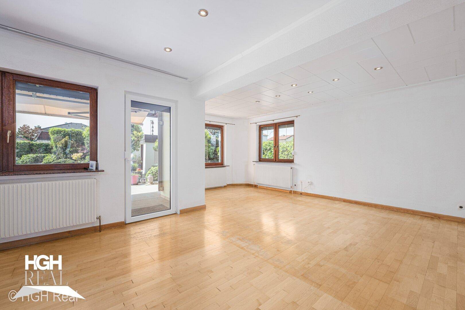 Heller Wohnraum mit Parkettboden, großen Fenstern und Zugang zur Terrasse.