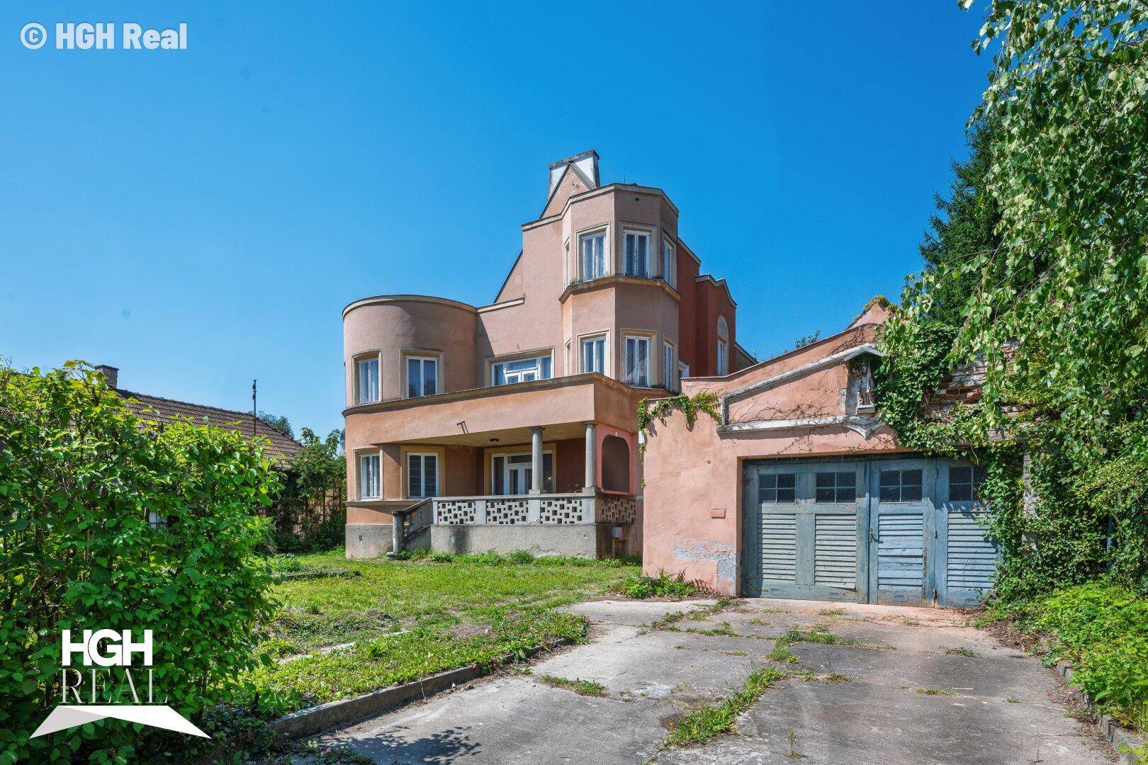 Historisches Gebäude mit Garage und großem Vorgarten unter blauem Himmel.