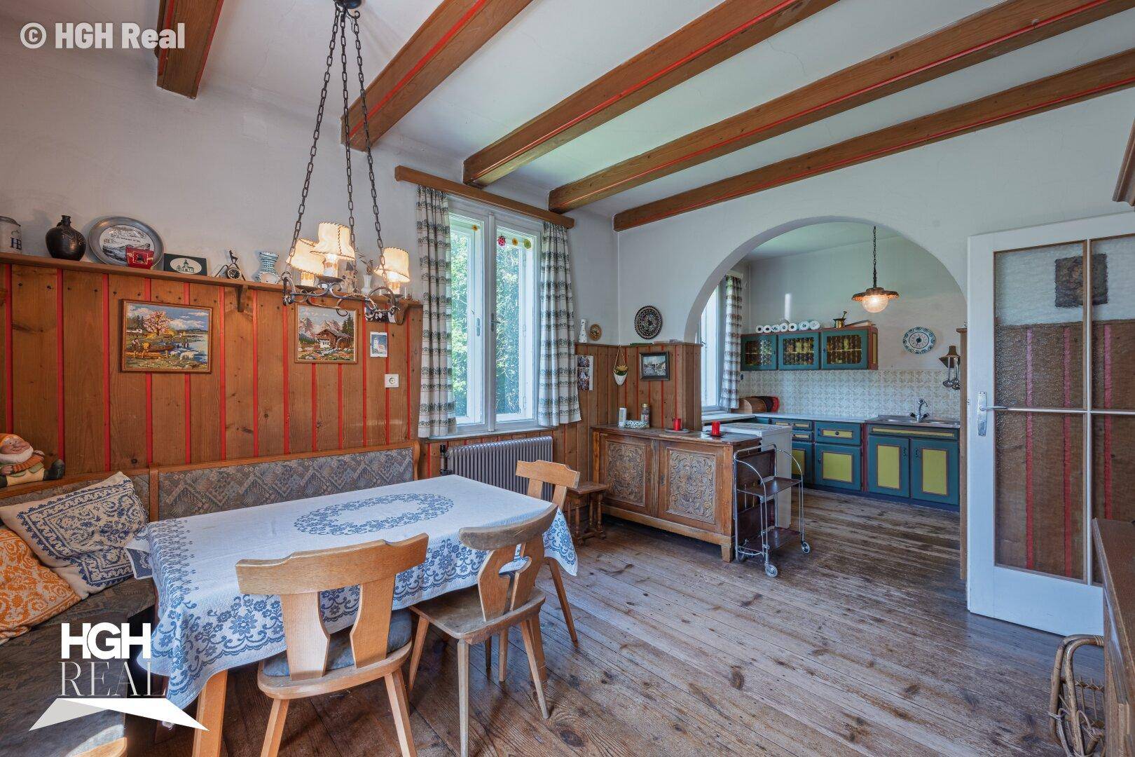 Rustikaler Wohn-Essbereich mit Holzbalken, Holzboden und einer traditionellen Küche im Hintergrund.