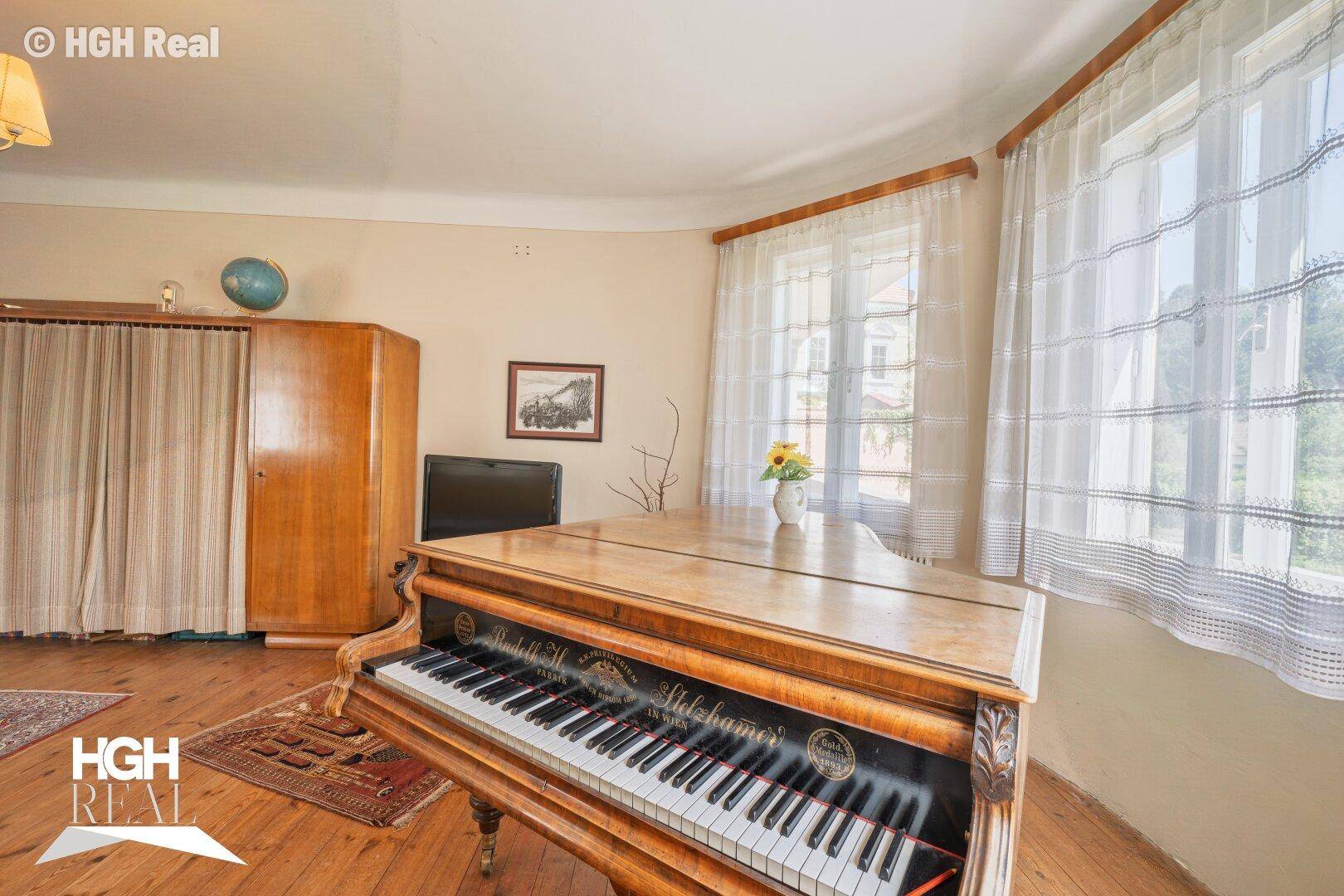 Helles Wohnzimmer mit Klavier, Holzboden und großen Fenstern.