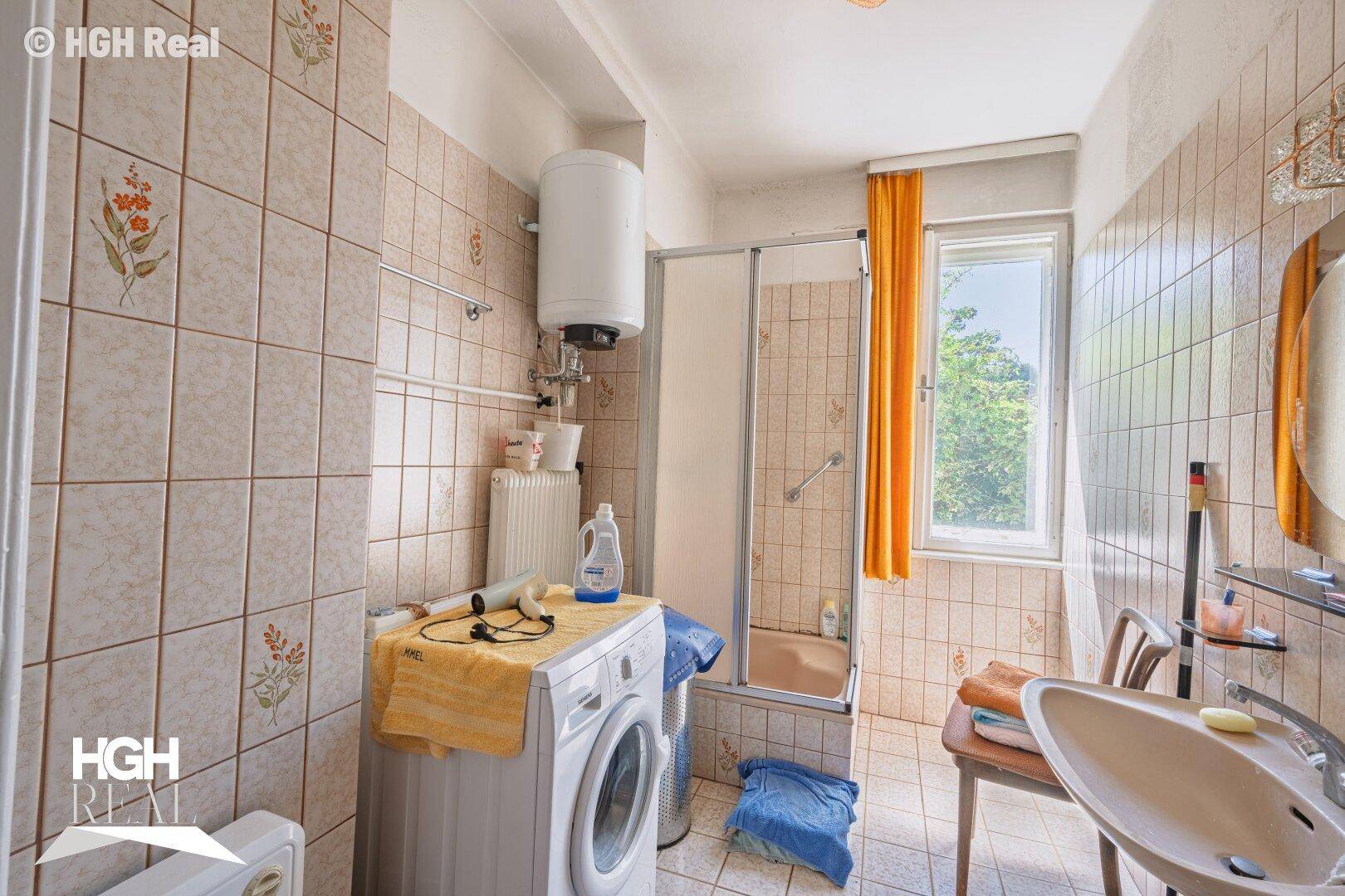Badezimmer mit beigen Fliesen, Dusche und Waschmaschine.