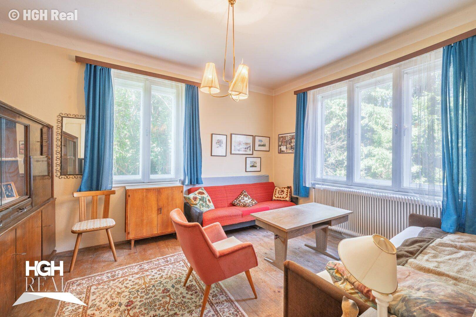 Gemütliches Schlafzimmer mit Holzboden, blauen Vorhängen und Blick ins Grüne.