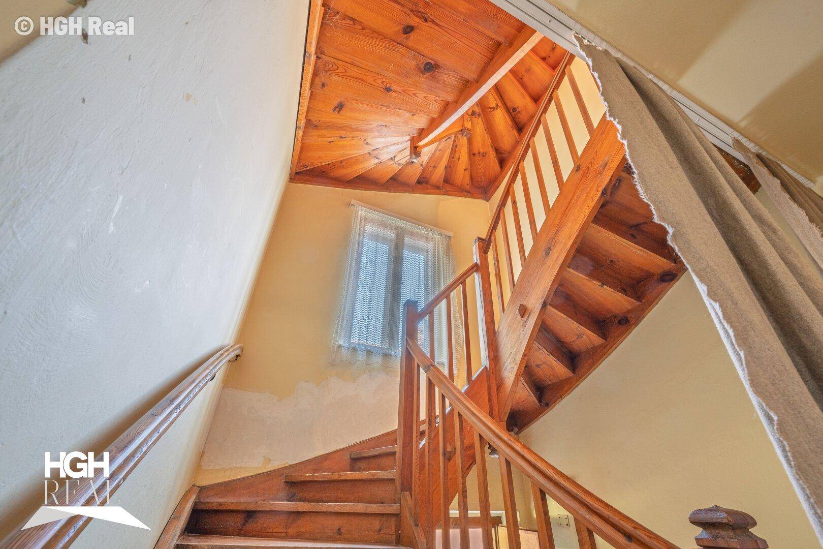 Holztreppe mit Geländer und Fenster, die die oberen Stockwerke verbindet.