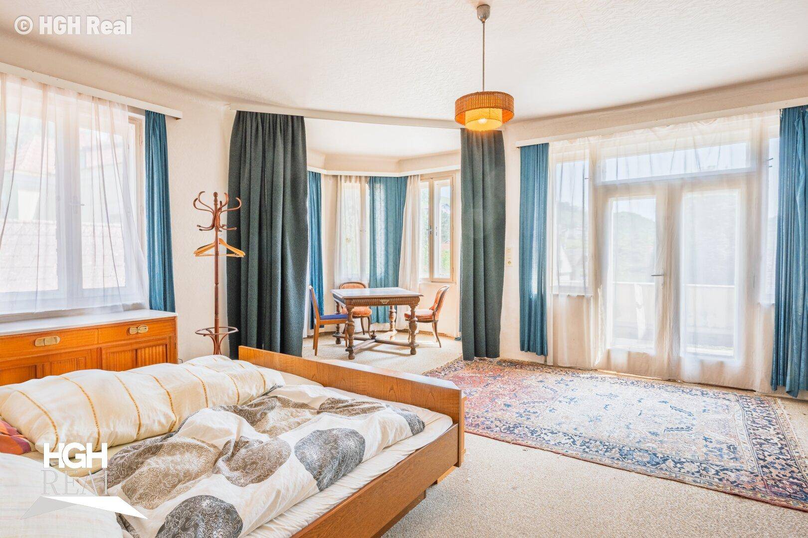 Geräumiges Schlafzimmer mit Teppichboden, großen Fenstern und Zugang zu einem kleinen Balkon.