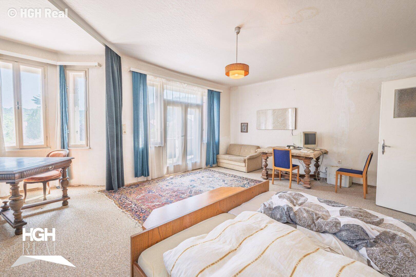 Großes Schlafzimmer mit Teppichboden, blauen Vorhängen und viel Tageslicht.