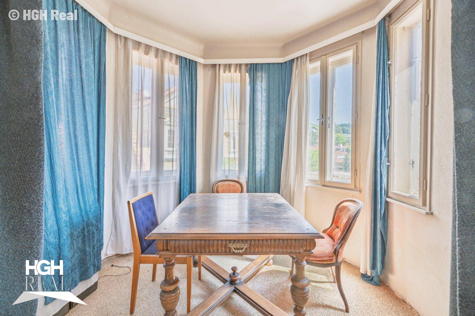 Kleiner Essbereich mit Holztisch, Stühlen und blauen Vorhängen.