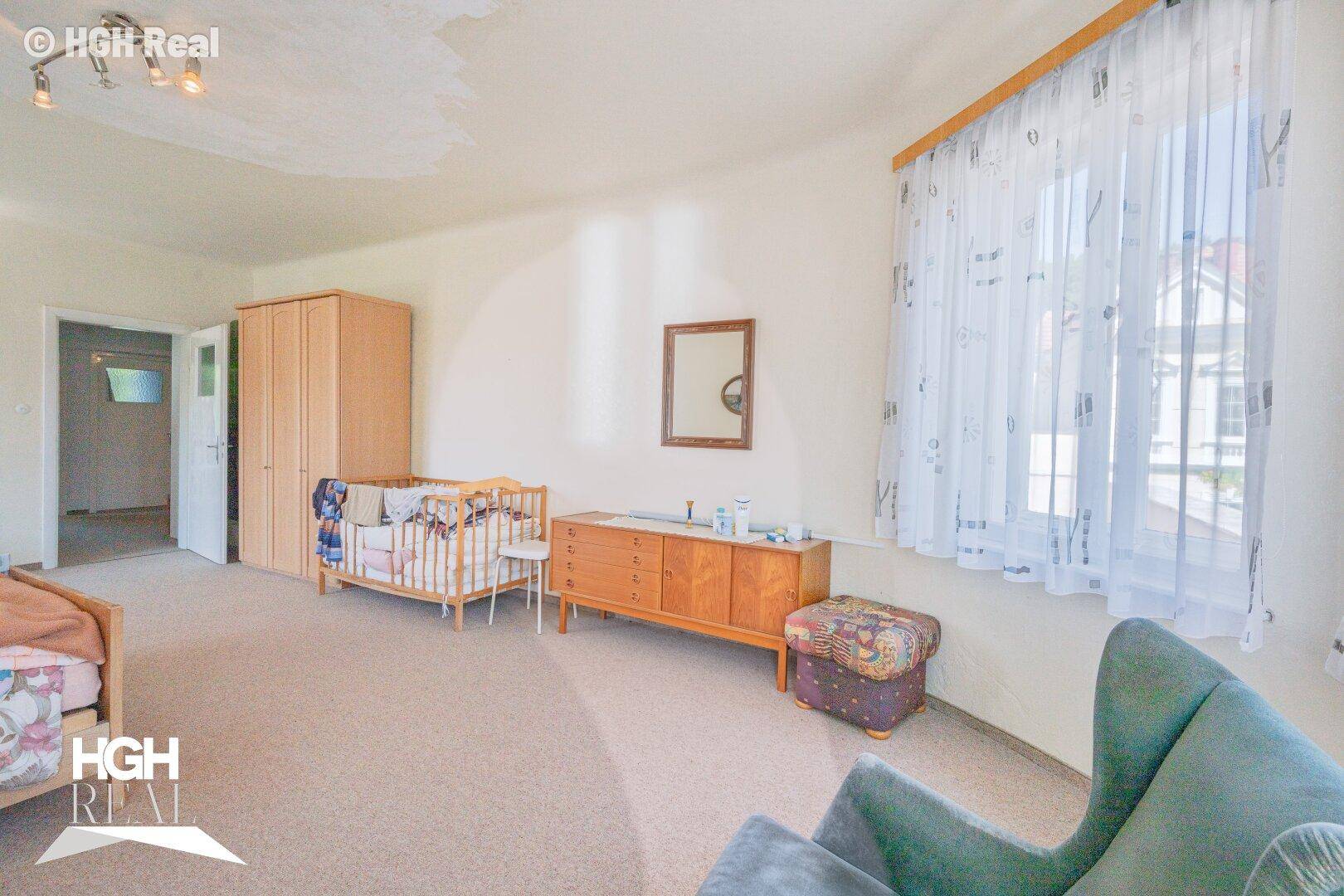 Schlafzimmer mit Teppichboden, einem Kinderbett und einem Fenster mit Vorhängen.