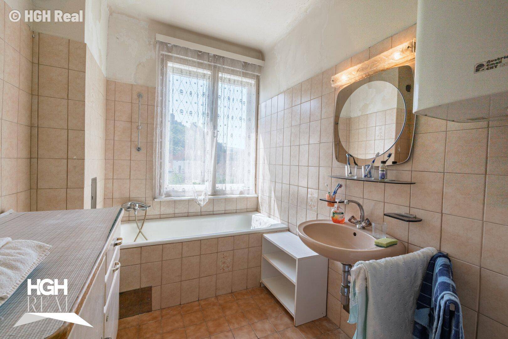 Badezimmer mit beigefarbenen Fliesen, Badewanne, Waschbecken und einem Fenster.