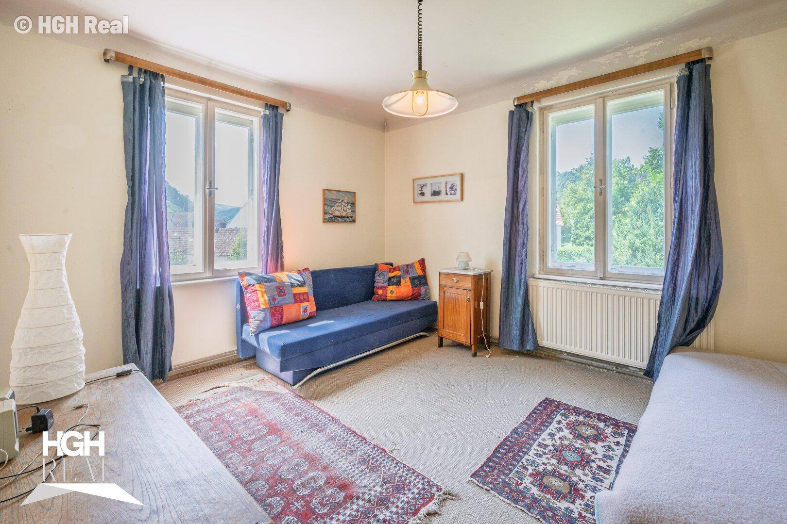 Schlafzimmer mit Teppichboden, blauen Vorhängen und Blick ins Grüne.