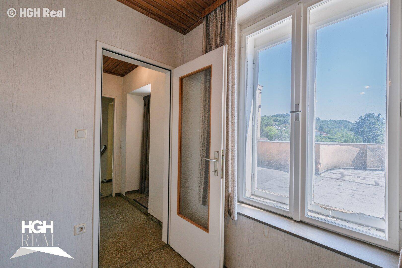 Kleiner Innenbereich mit Zugang zu einer großen Dachterrasse und Blick ins Grüne.