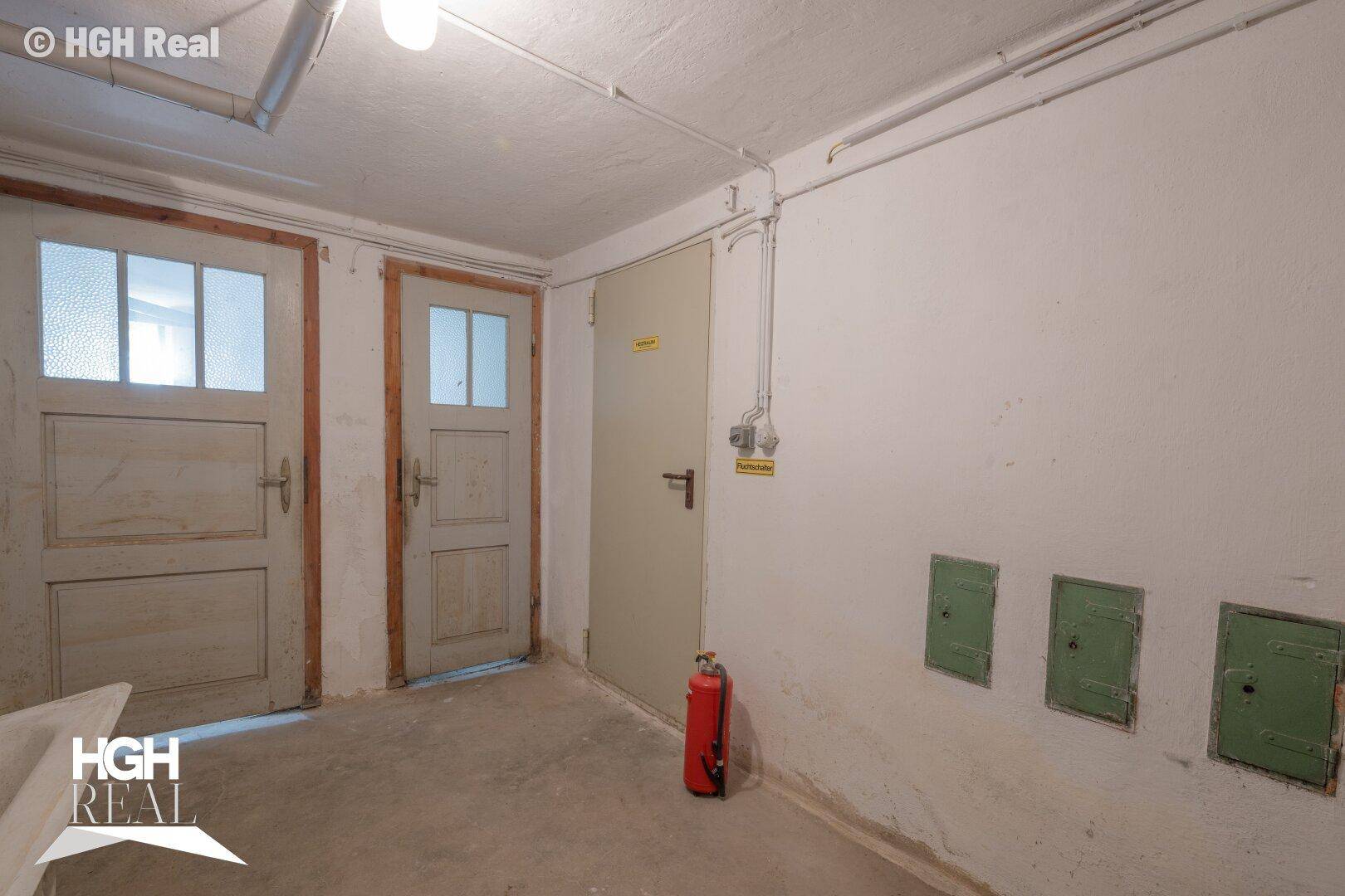 Kellerflur mit mehreren Türen, Betonboden und einem Feuerlöscher.
