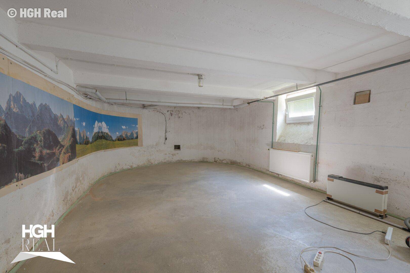 Großer Kellerraum mit Betonboden, einem Wandbild und einem kleinen Fenster.