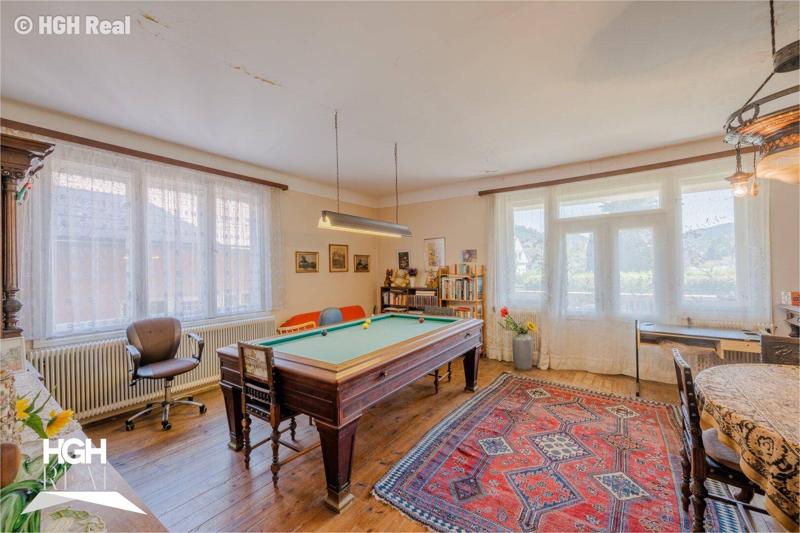 Geräumiges Wohnzimmer mit Billardtisch, Holzboden und großen Fenstern.