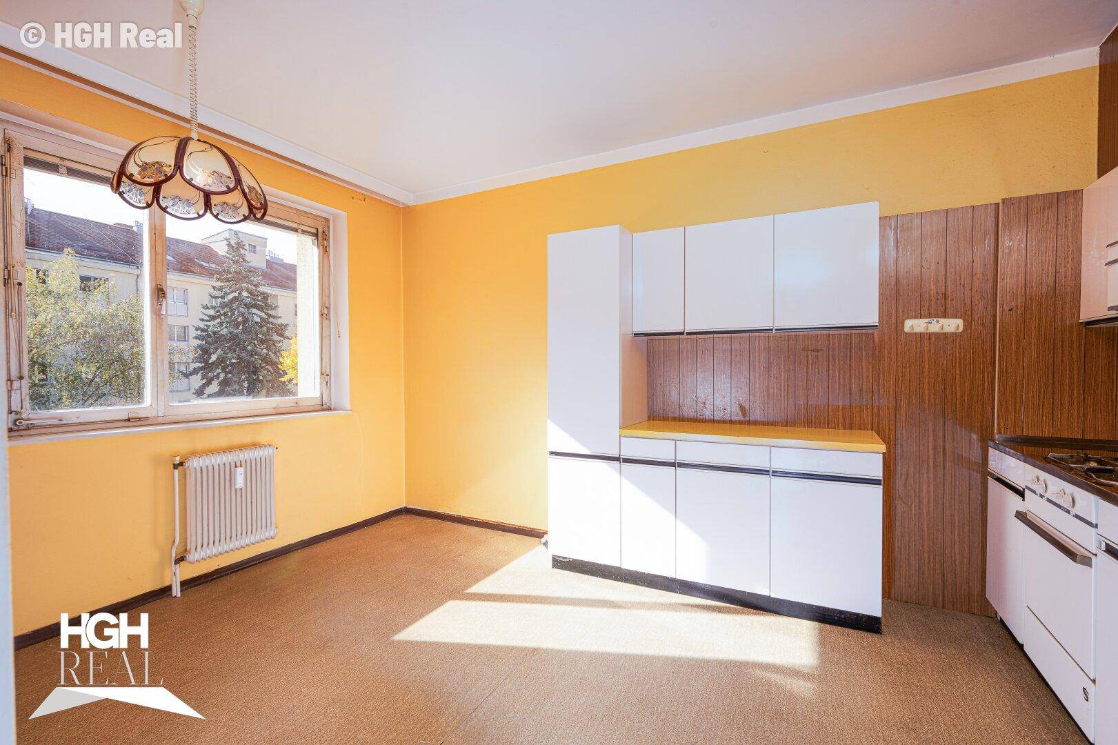 Küche mit gelben Wänden, älteren weißen Einbauschränken und einem Fenster mit Heizkörper.