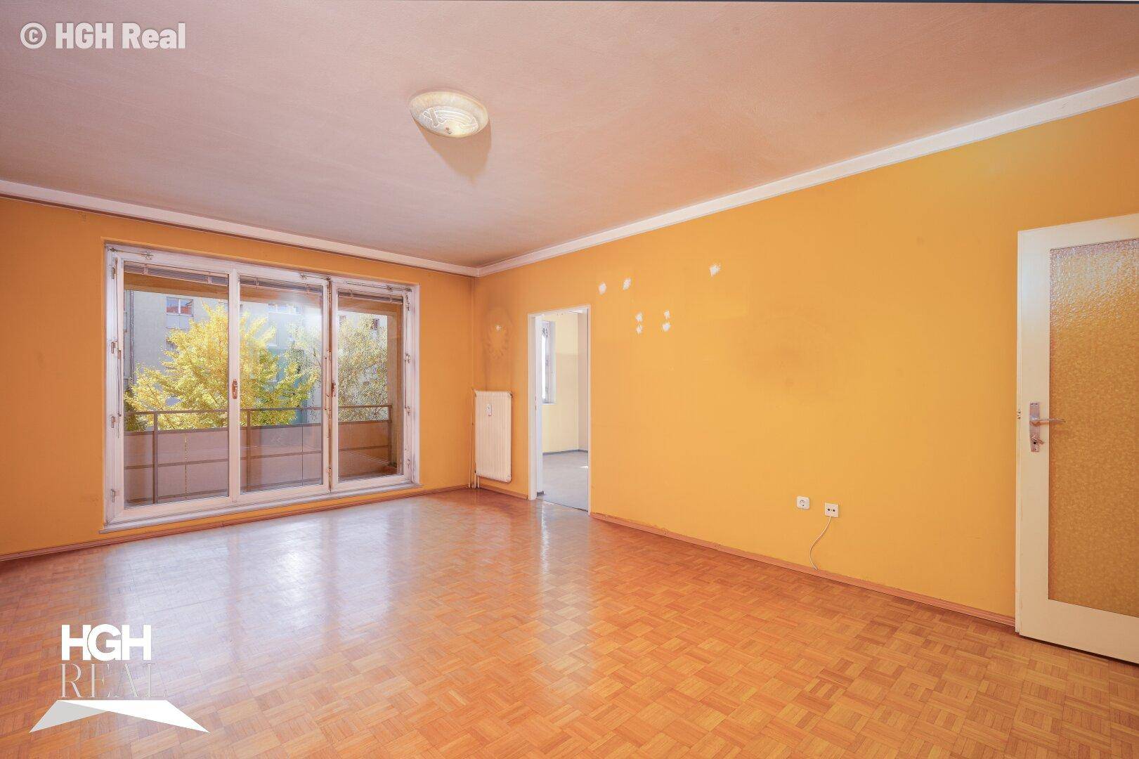 Helles Wohnzimmer mit gelben Wänden, Parkettboden und großem Schiebefenster zum Balkon.