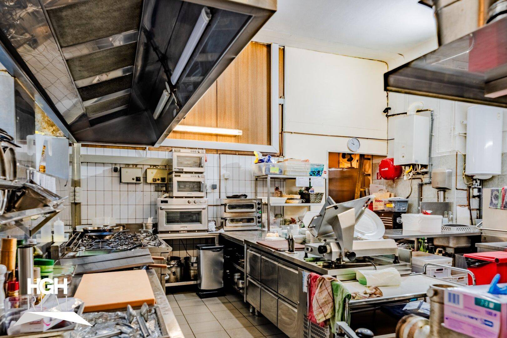 Professionelle Großküche mit Edelstahlgeräten, Dunstabzugshauben und gefliesten Wänden für den Restaurantbetrieb.