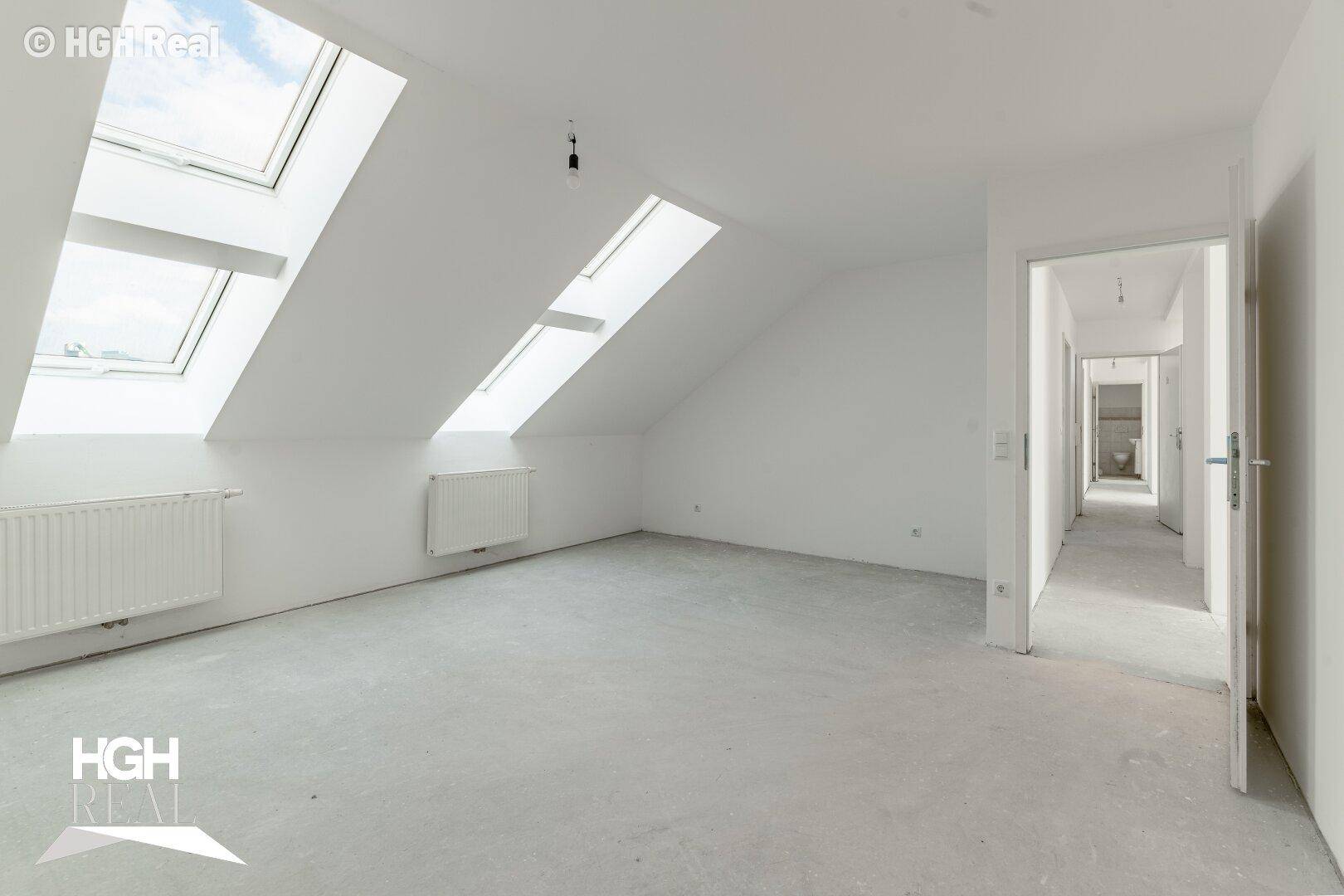Geräumiger Dachbodenraum mit schrägen Wänden und mehreren Dachfenstern für viel Tageslicht.