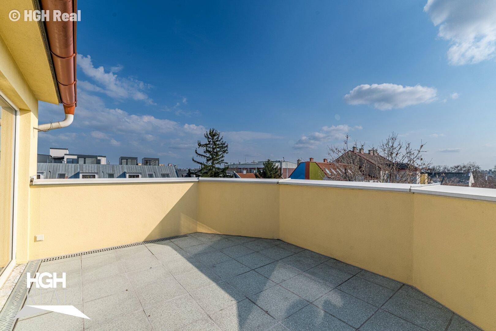 Geräumige Terrasse mit gelber Wand, Fliesenboden und weitem Blick über die städtische Umgebung.
