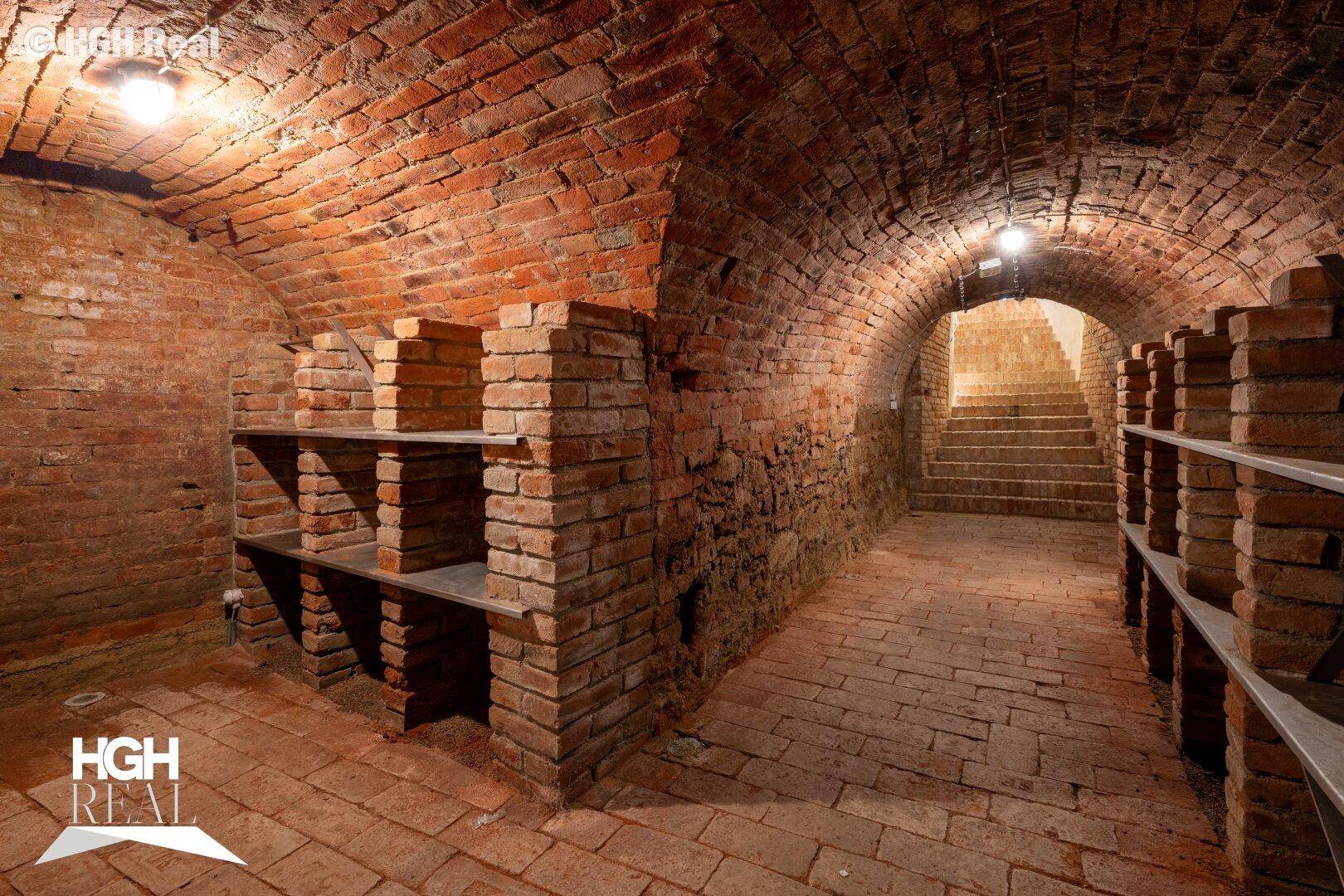 Historischer Gewölbekeller mit Ziegelwänden und -boden, ausgestattet mit Regalen für Lagerzwecke.