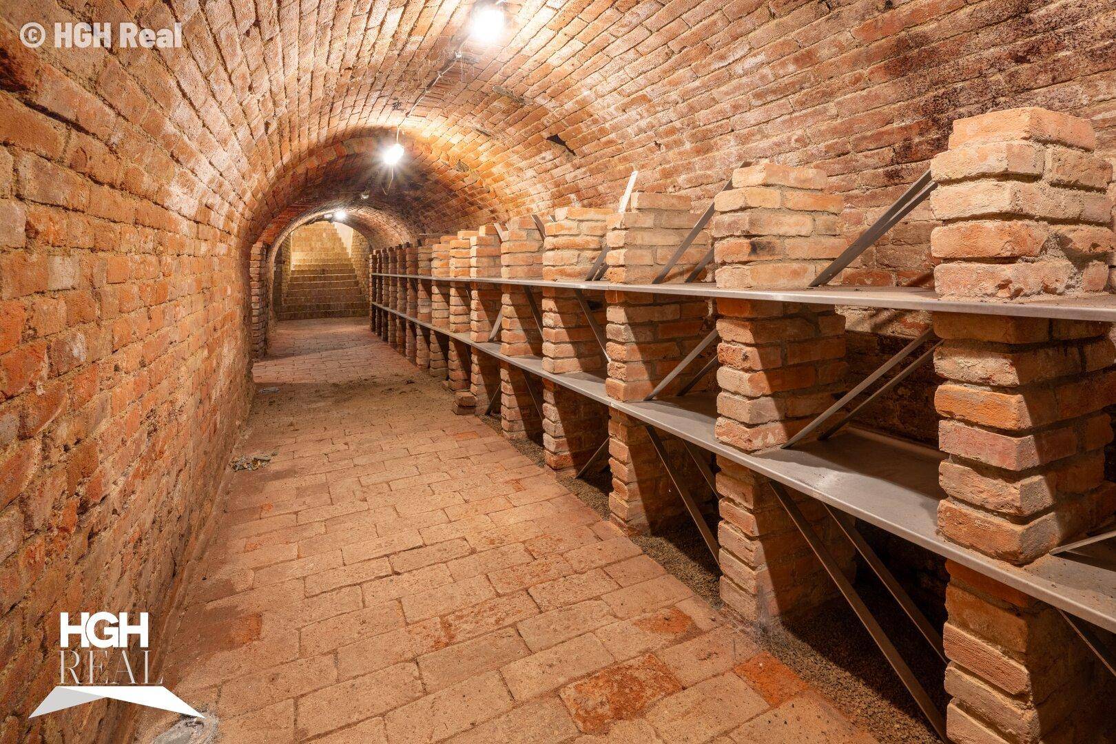 Historischer Gewölbekeller mit Ziegelwänden und -boden, ausgestattet mit Regalen für Lagerzwecke.