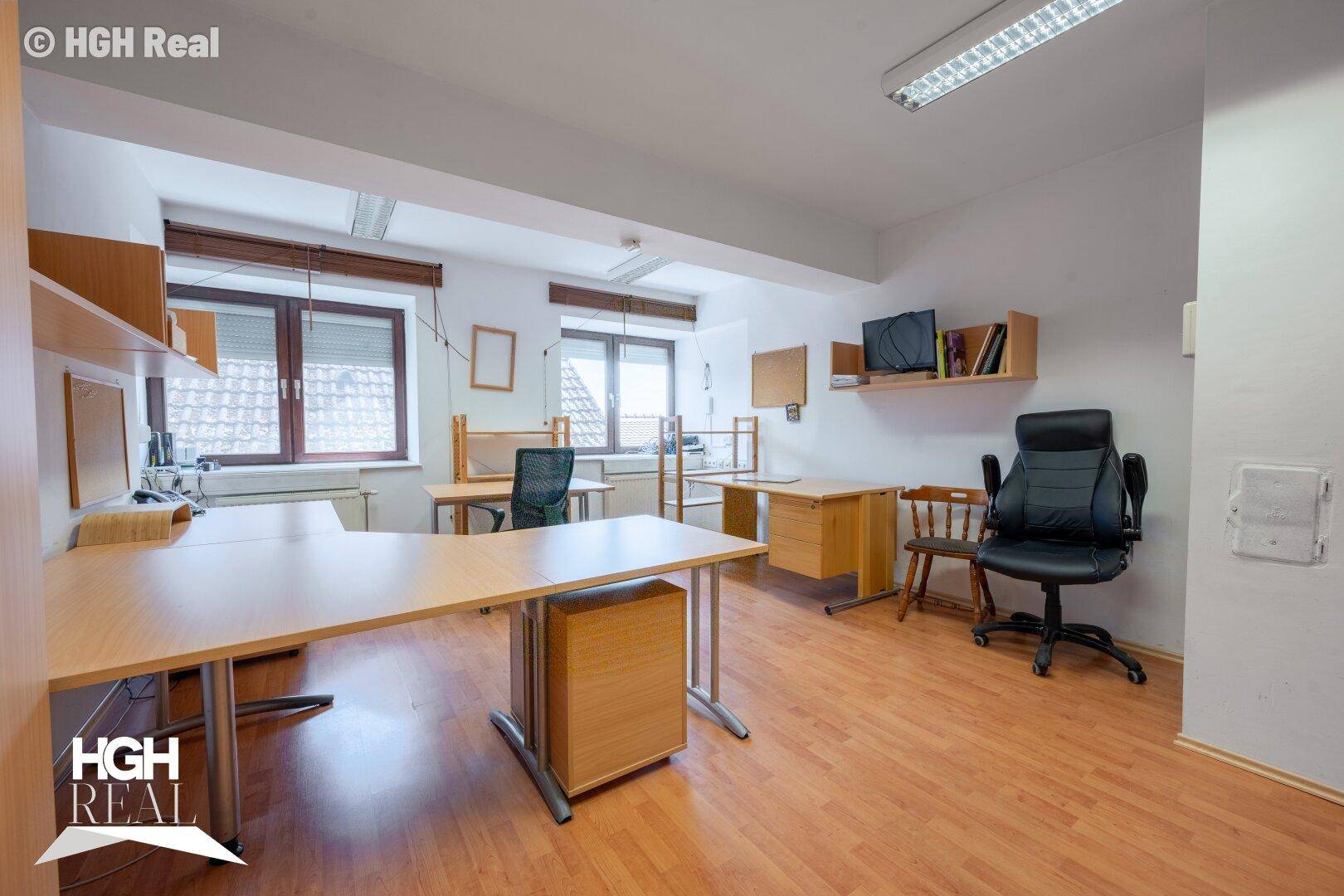 Helles Büro mit mehreren Schreibtischen, Bürostühlen und Holzregalen, ausgestattet mit Fenstern.