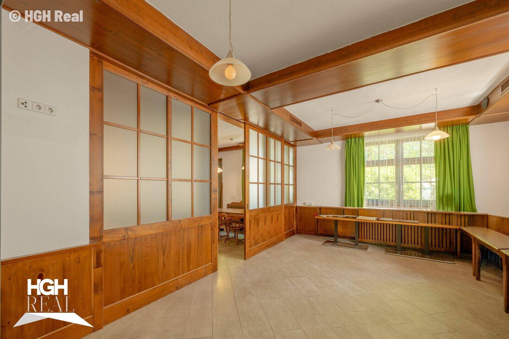 Heller Raum mit Holzvertäfelung, Milchglas-Trennwänden und Blick ins Grüne durch die Fenster.