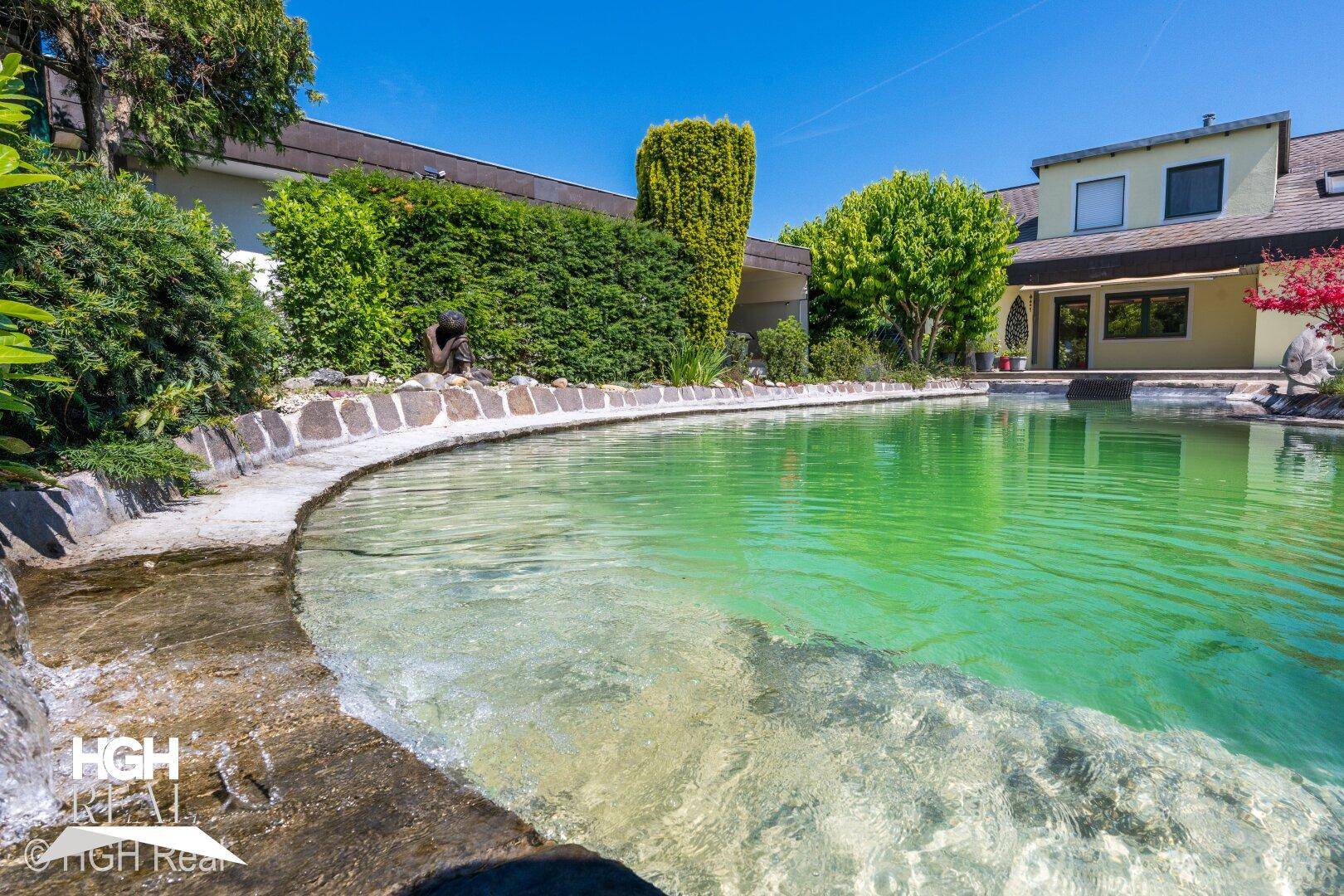 Gepflegter Gartenbereich mit einem großen Teich, hohen Hecken und dem Haus im Hintergrund.