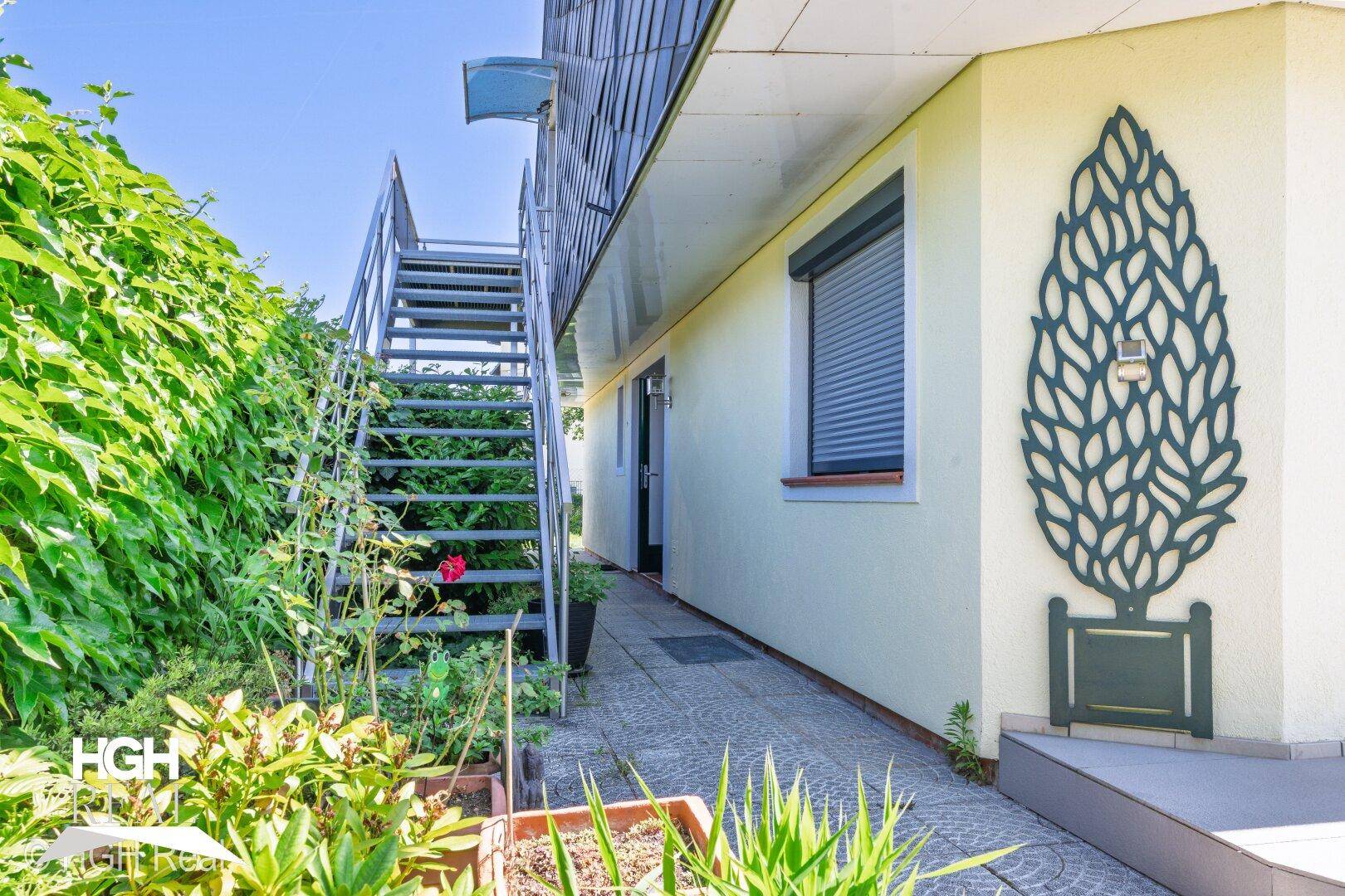 Außenbereich des Hauses mit Treppe zum Obergeschoss und üppiger Begrünung.