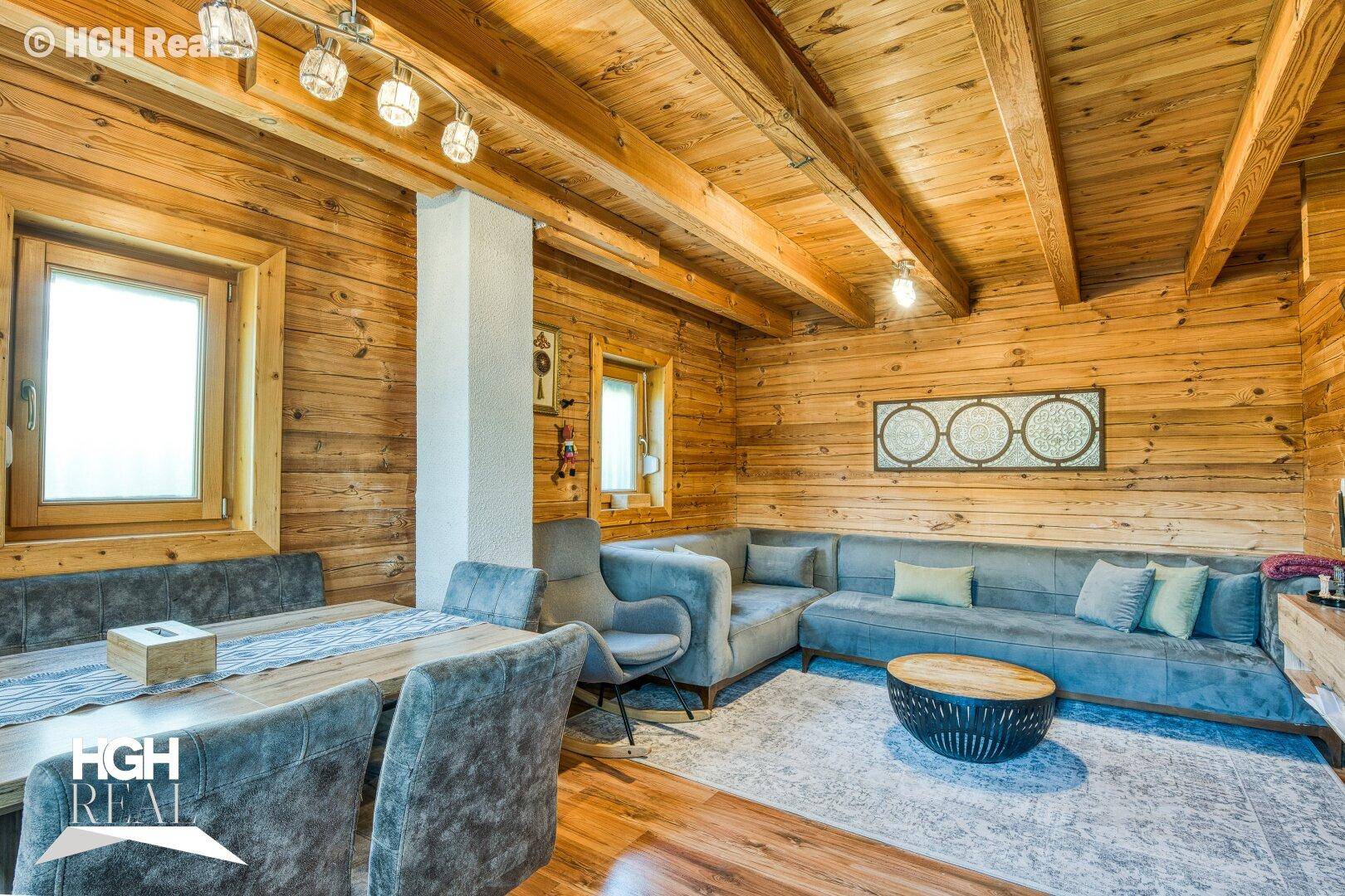 Geräumiger Wohn-Essbereich mit Holzwänden, Holzbalkendecke und bequemen Sitzgelegenheiten.