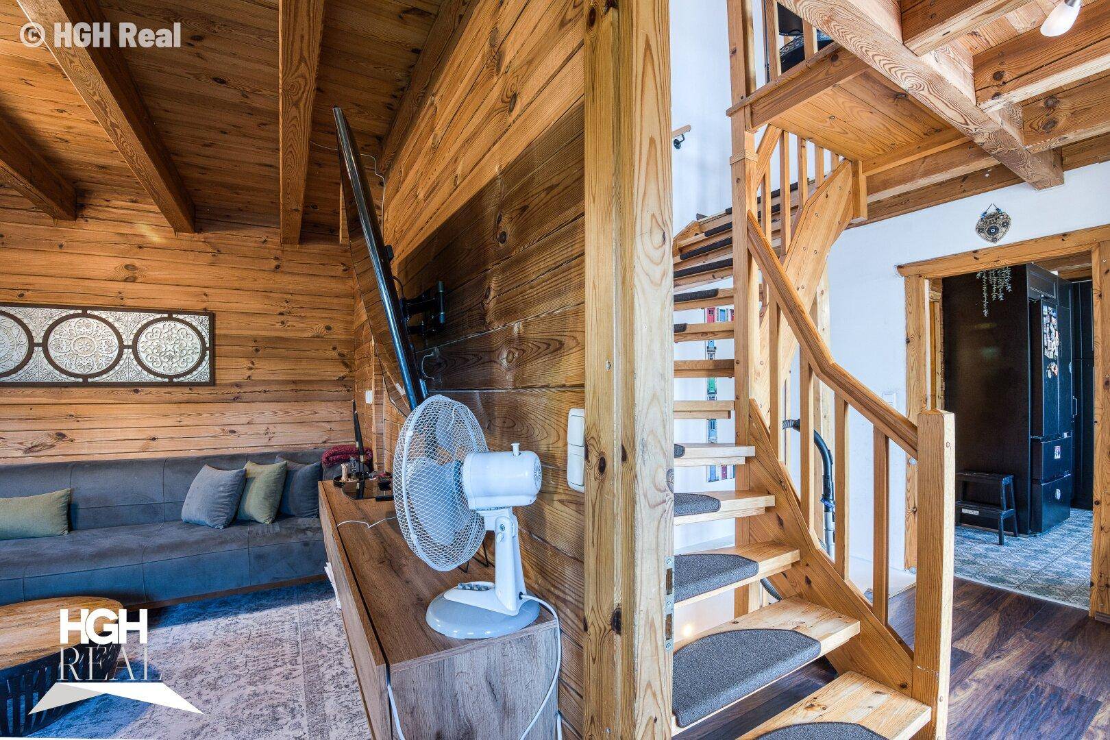 Wohnzimmer mit Sofa, Holztreppe und rustikalen Holzwänden sowie Holzbalkendecke.