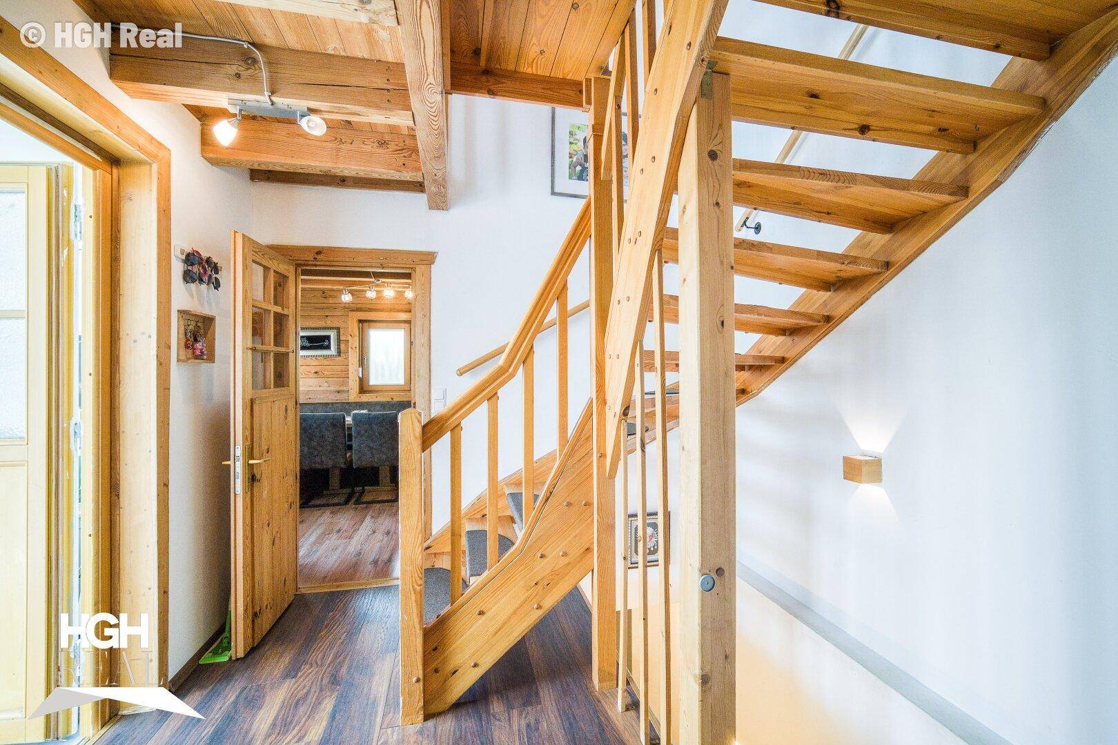 Heller Flur mit Holztreppe, Holztüren und sichtbaren Deckenbalken, die zu den Wohnbereichen führen.