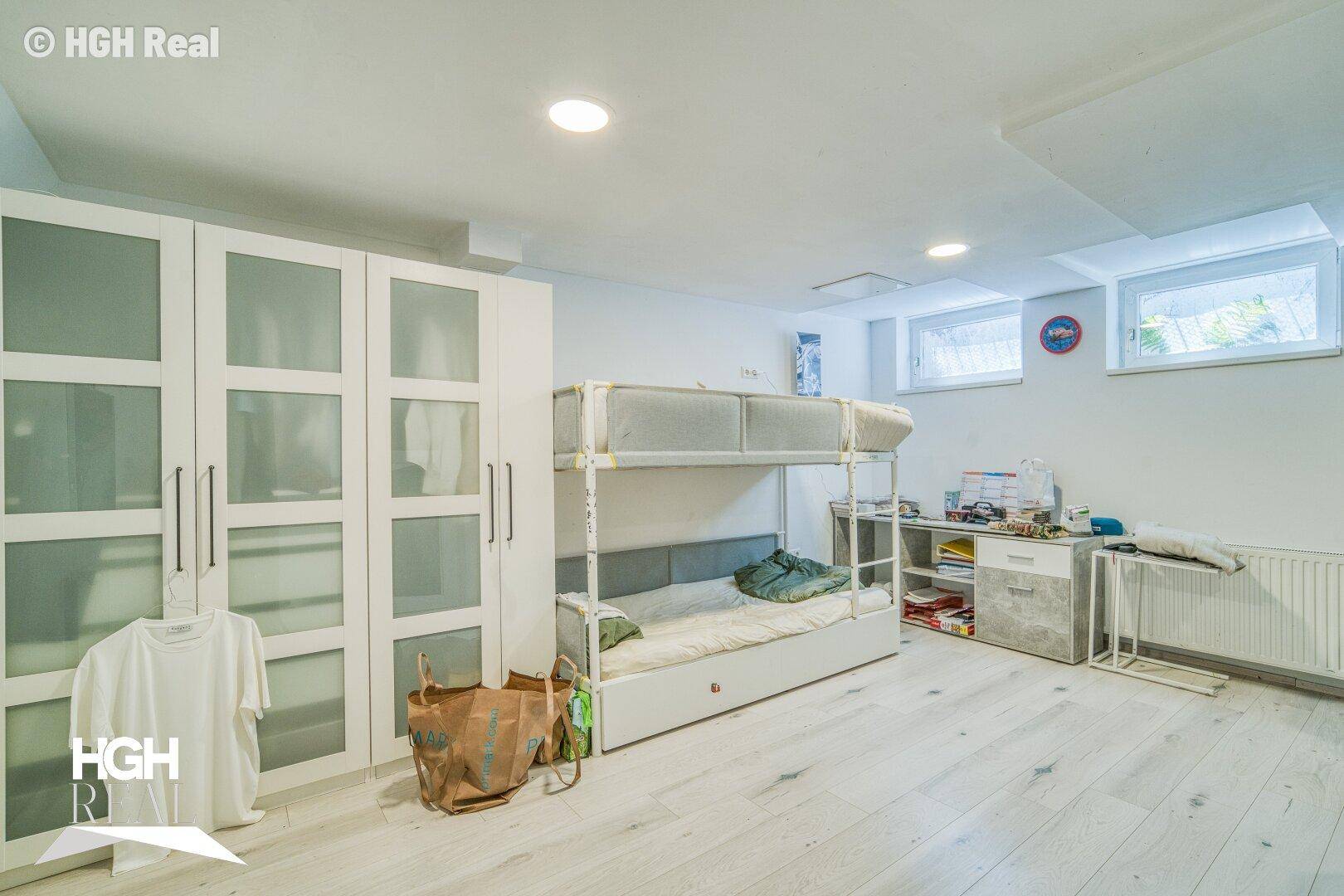 Geräumiger Kellerraum mit Etagenbett, Kleiderschrank und hellem Boden, nutzbar als Schlaf- oder Spielzimmer.