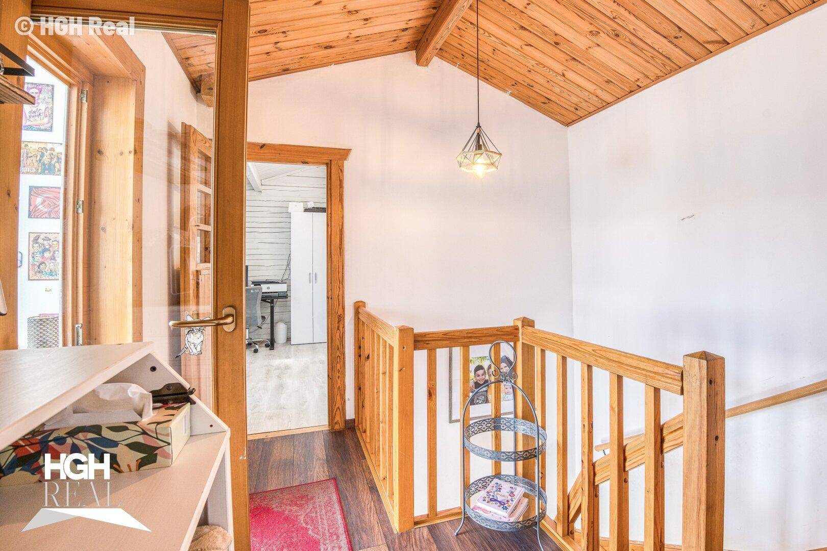 Heller Flur im Obergeschoss mit Holzgeländer und schräger Holzdecke, die zu weiteren Räumen führt.