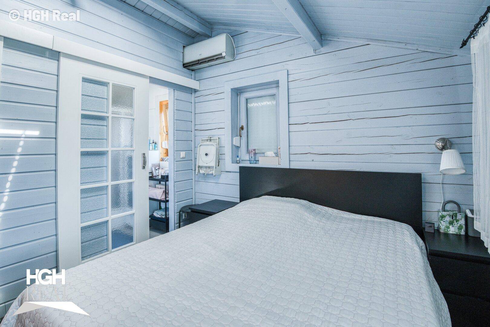 Schlafzimmer mit hellblauen Holzwänden, Holzbalkendecke, Doppelbett und Klimaanlage.