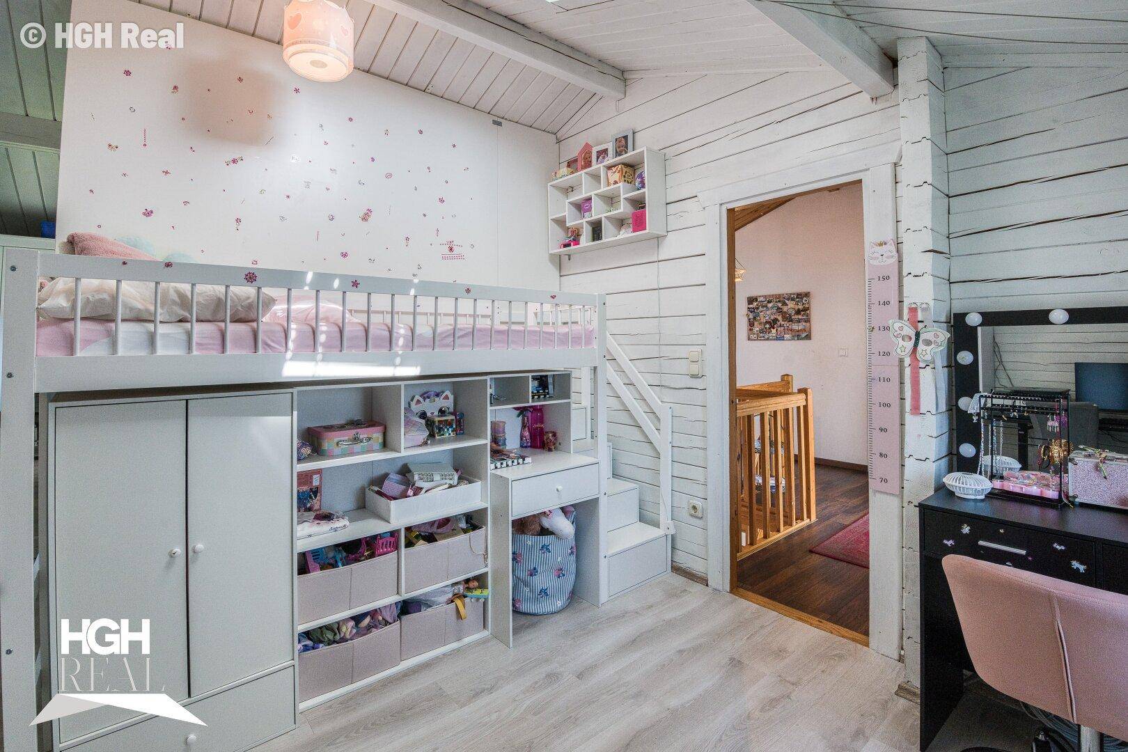Freundliches Kinderzimmer mit Hochbett, weißen Möbeln und Holzwänden unter einer Dachschräge.