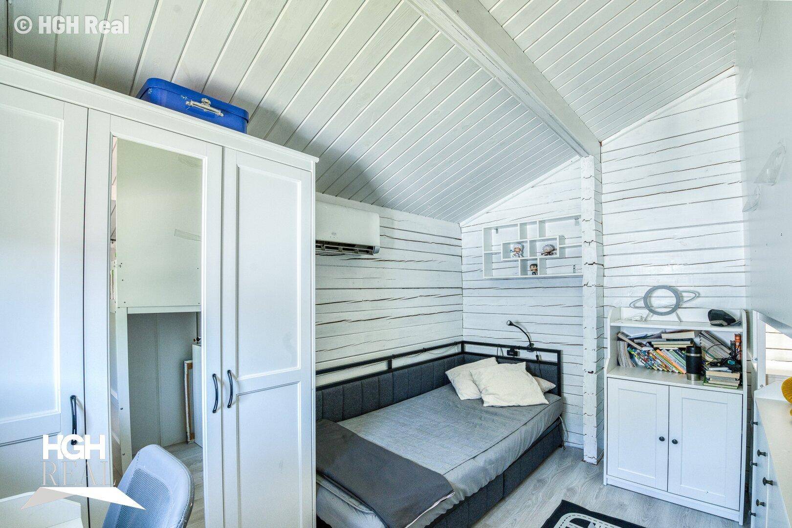 Kinderzimmer mit weißen Holzwänden, Dachschräge, Einzelbett und Klimaanlage.